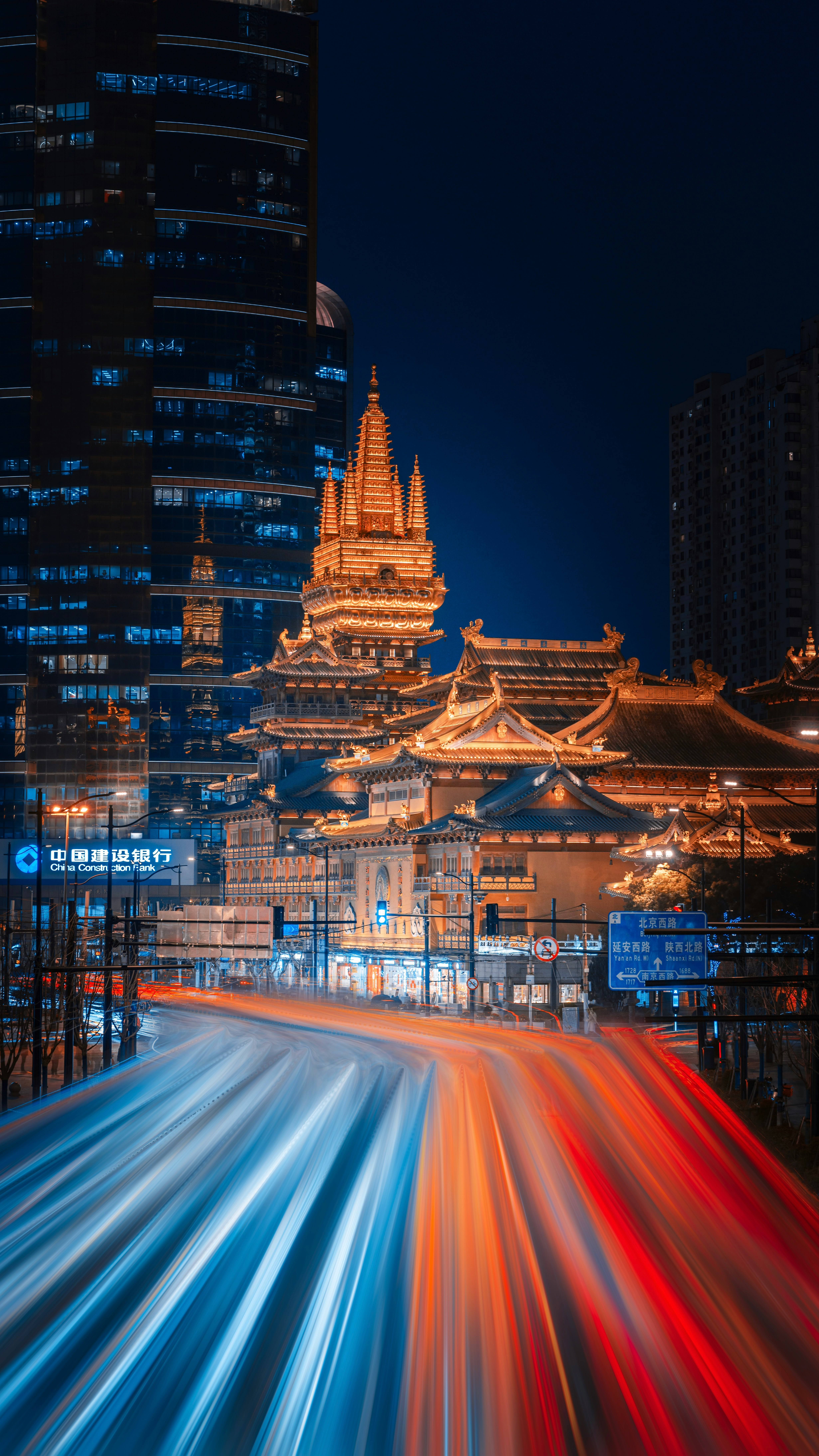 Cityscape at night with light trails and illuminated temple.