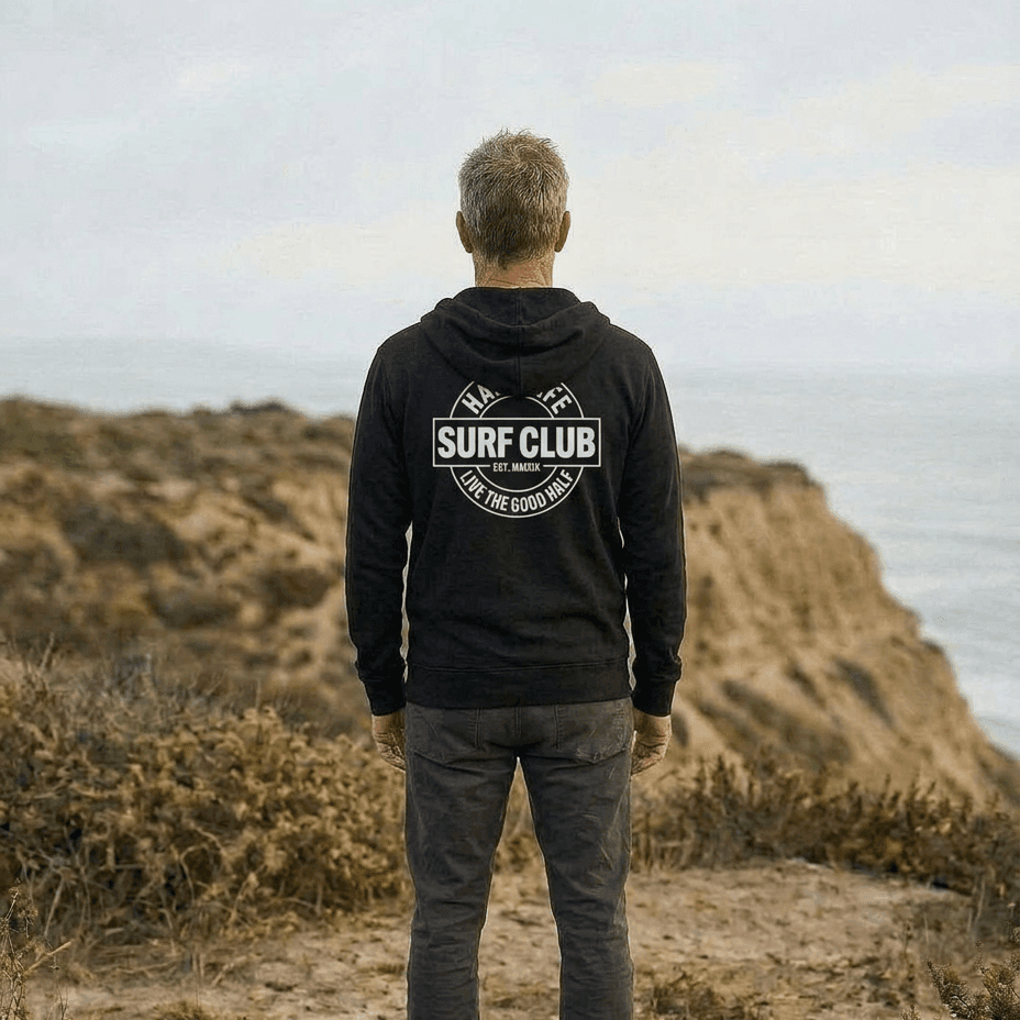 Person wearing a hoodie with 'Surf Club' logo standing on a coastal cliff.