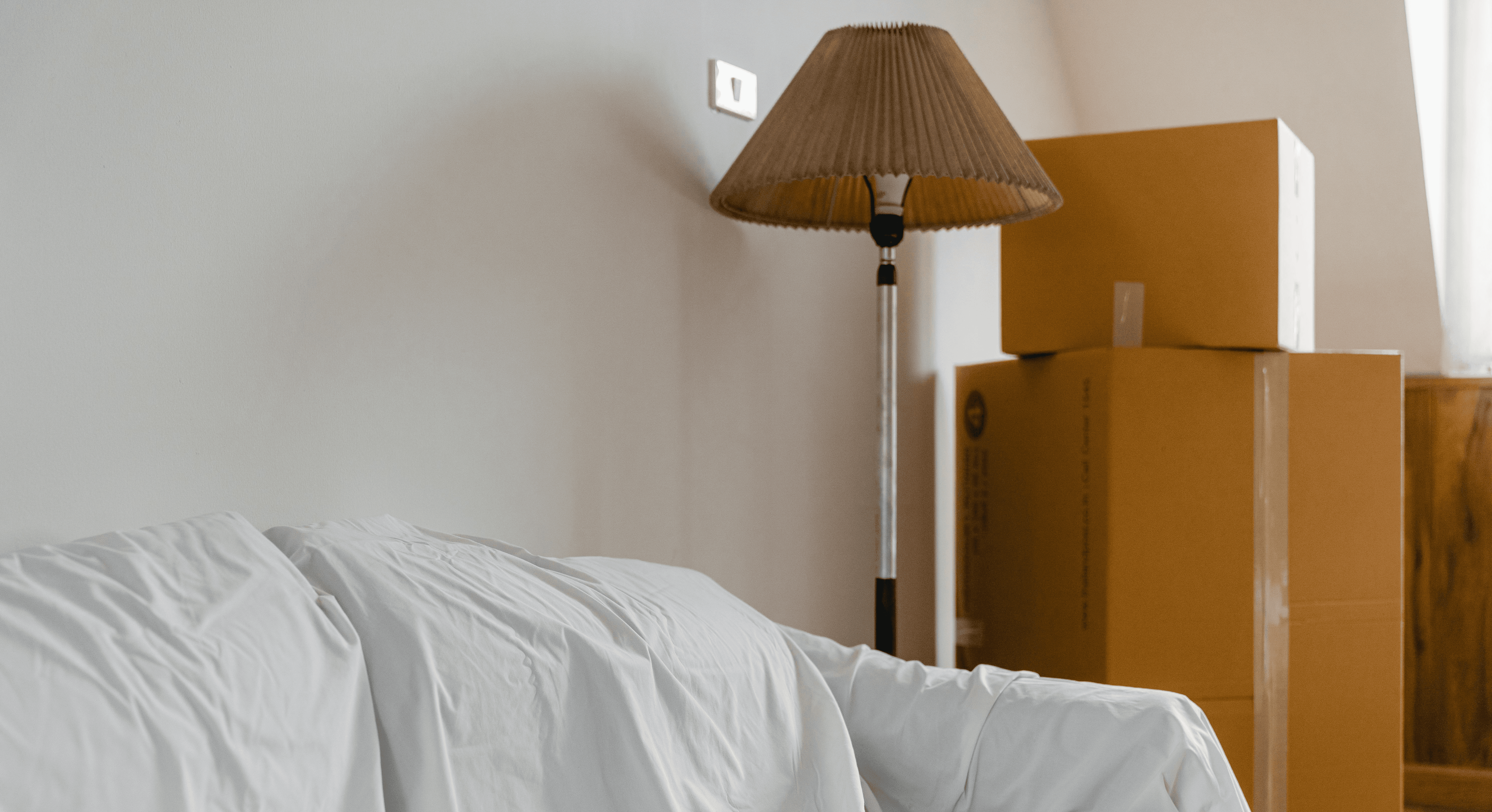 covered-with-sheet-sofa-and-floor-lamp-and-packed-cardboard-boxes-in-light-spaci - ketut-subiyanto (pexels)