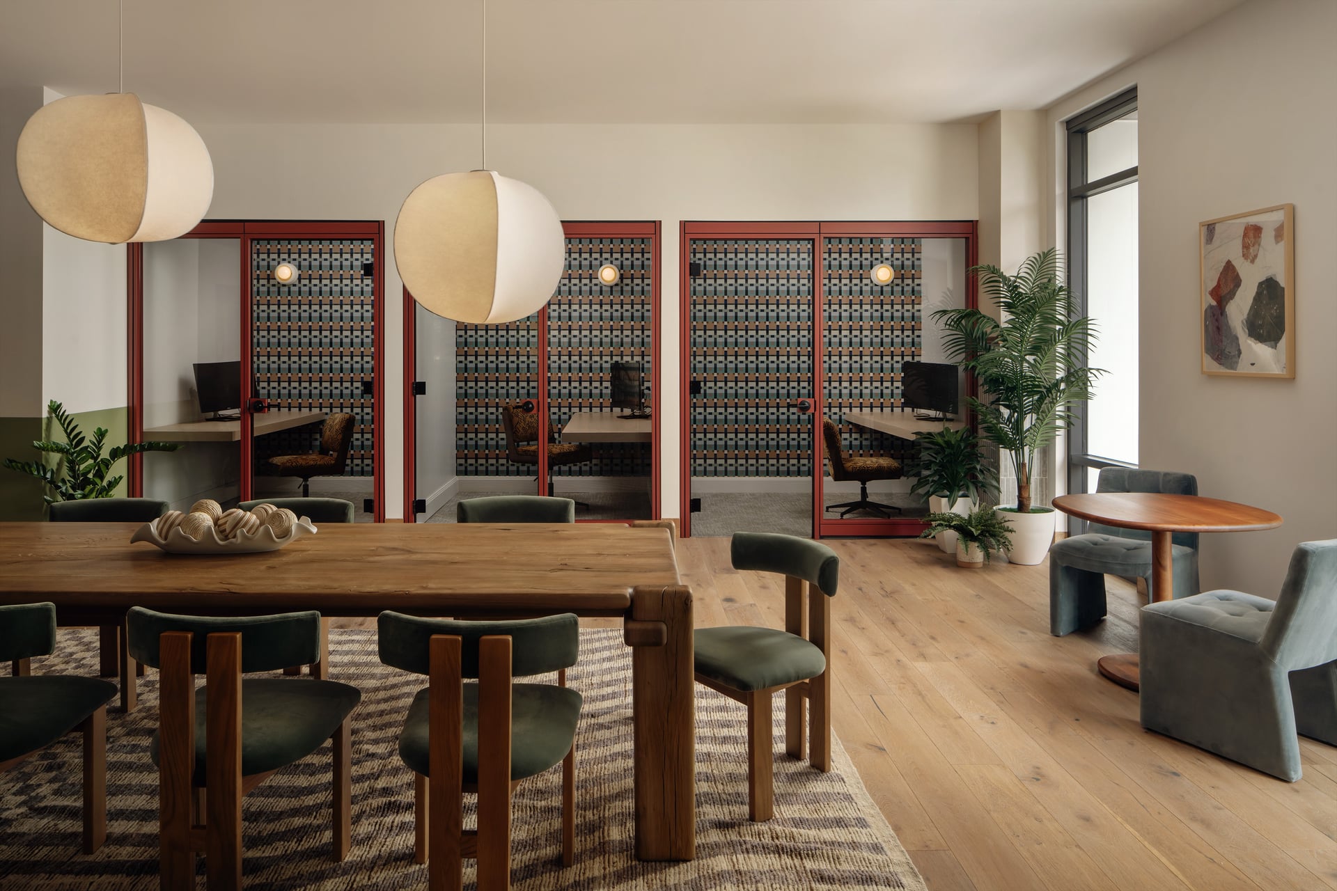 Modern commercial co-working interior design with wooden communal table, green upholstered chairs, globe pendant light fixtures, and private focus rooms.