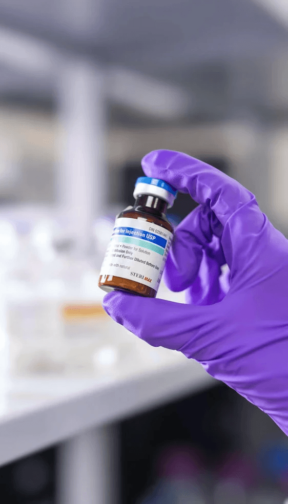 Close-up of a gloved hand holding a small vial of injectable medicine in a laboratory.