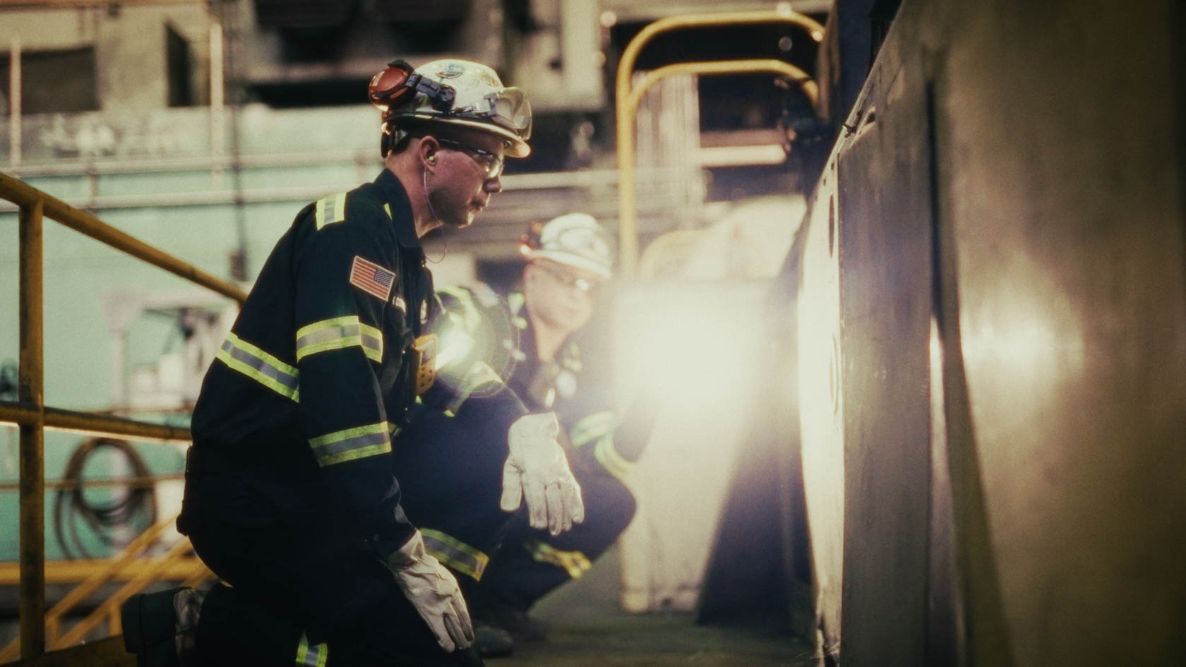 Gloved hand holding a cream card with a logo, wearing a gold bracelet and a blue gemstone flower ring against a red background.