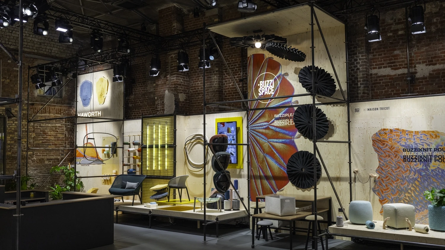 Haworth booth in a brick hall with scaffold structure, fabric panels, lounge furniture and spotlights.