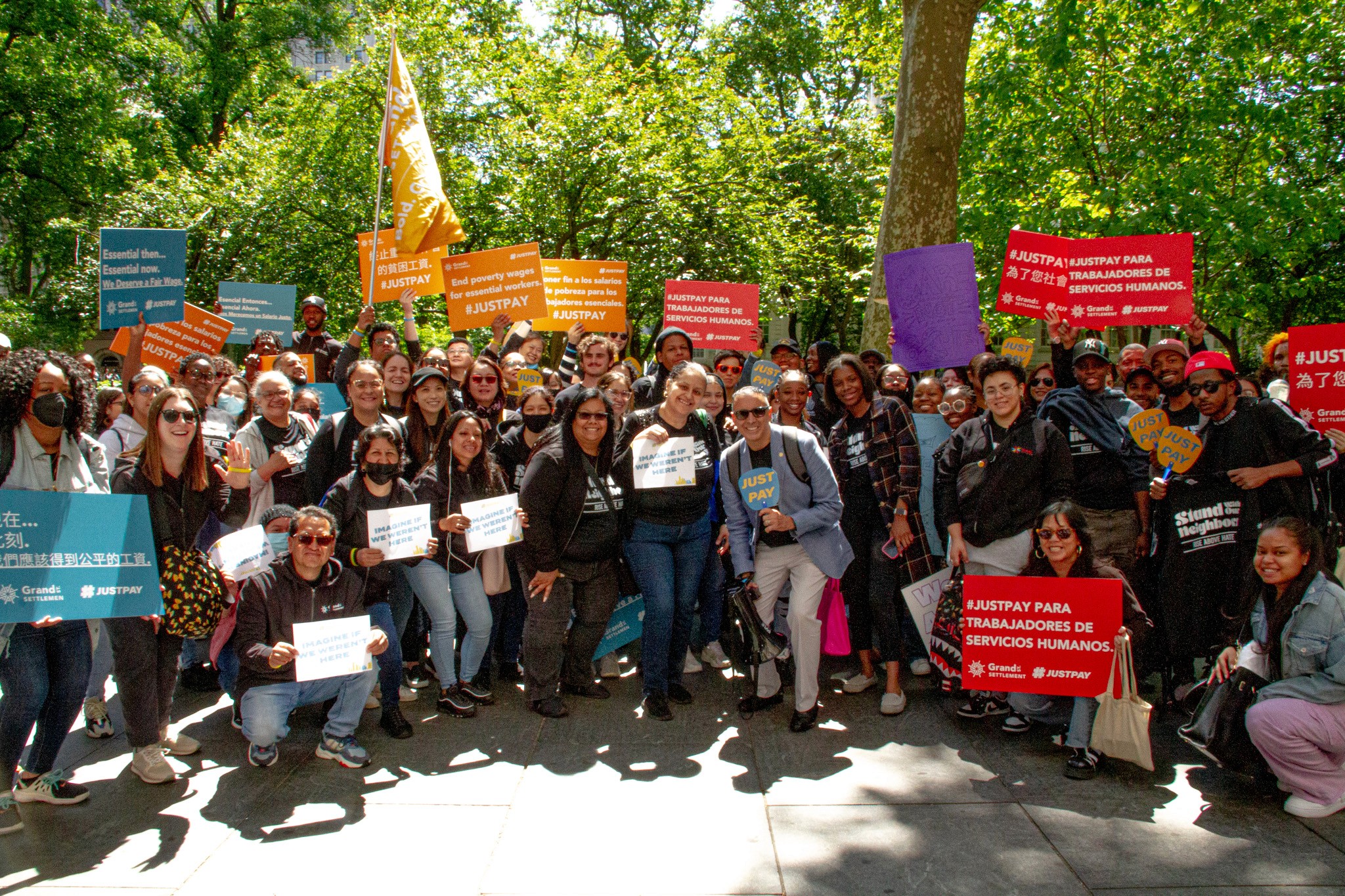 A group of Grand St. Settlement staff stand outside with signs advocacting for pay equity.