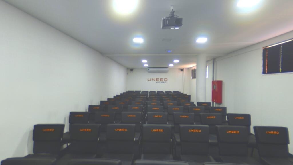 Auditório da UNEED com poltronas pretas estampadas e projetor