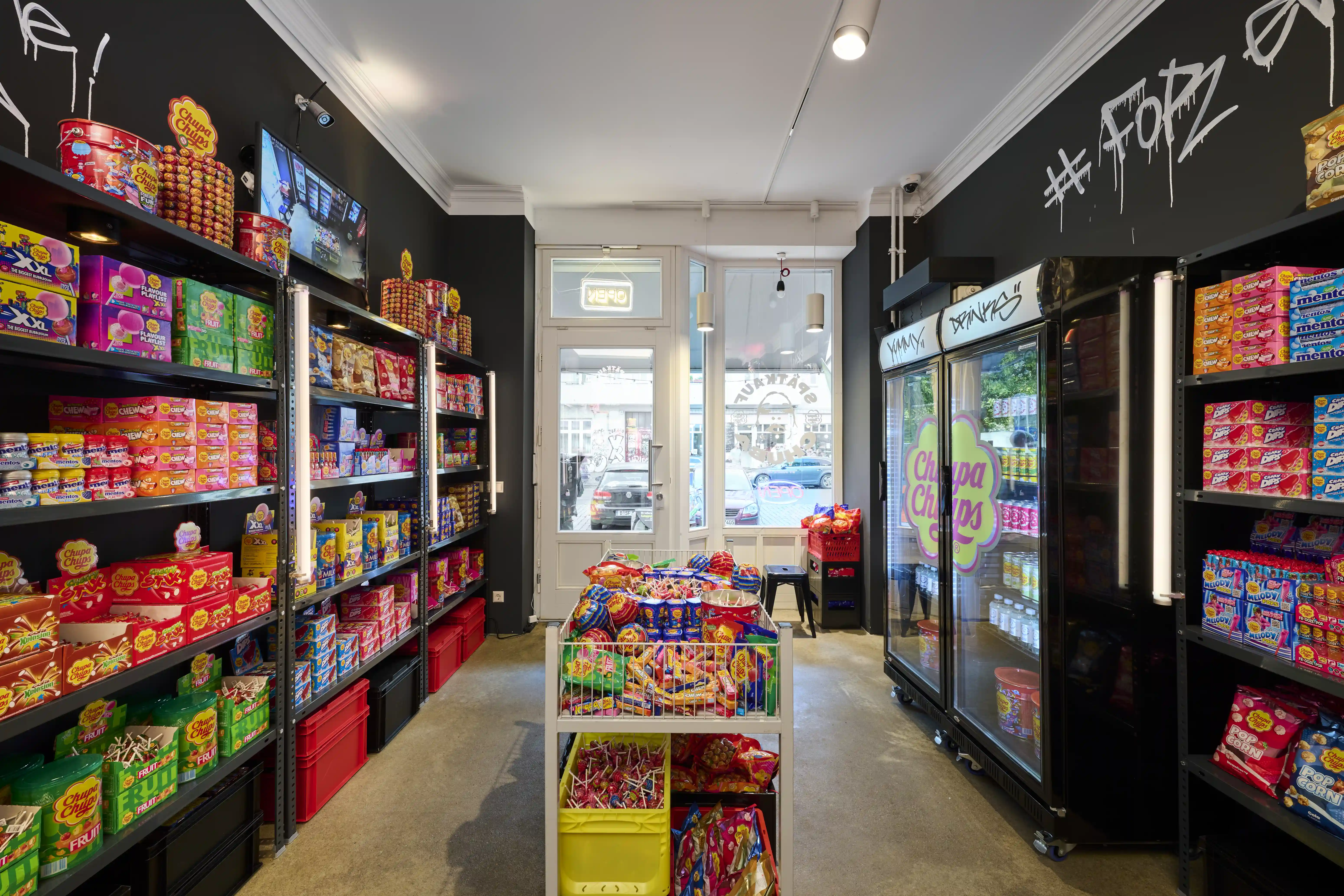 View through the candy-filled Spätkauf Chuba with shelves, branded fridge and window to the street.