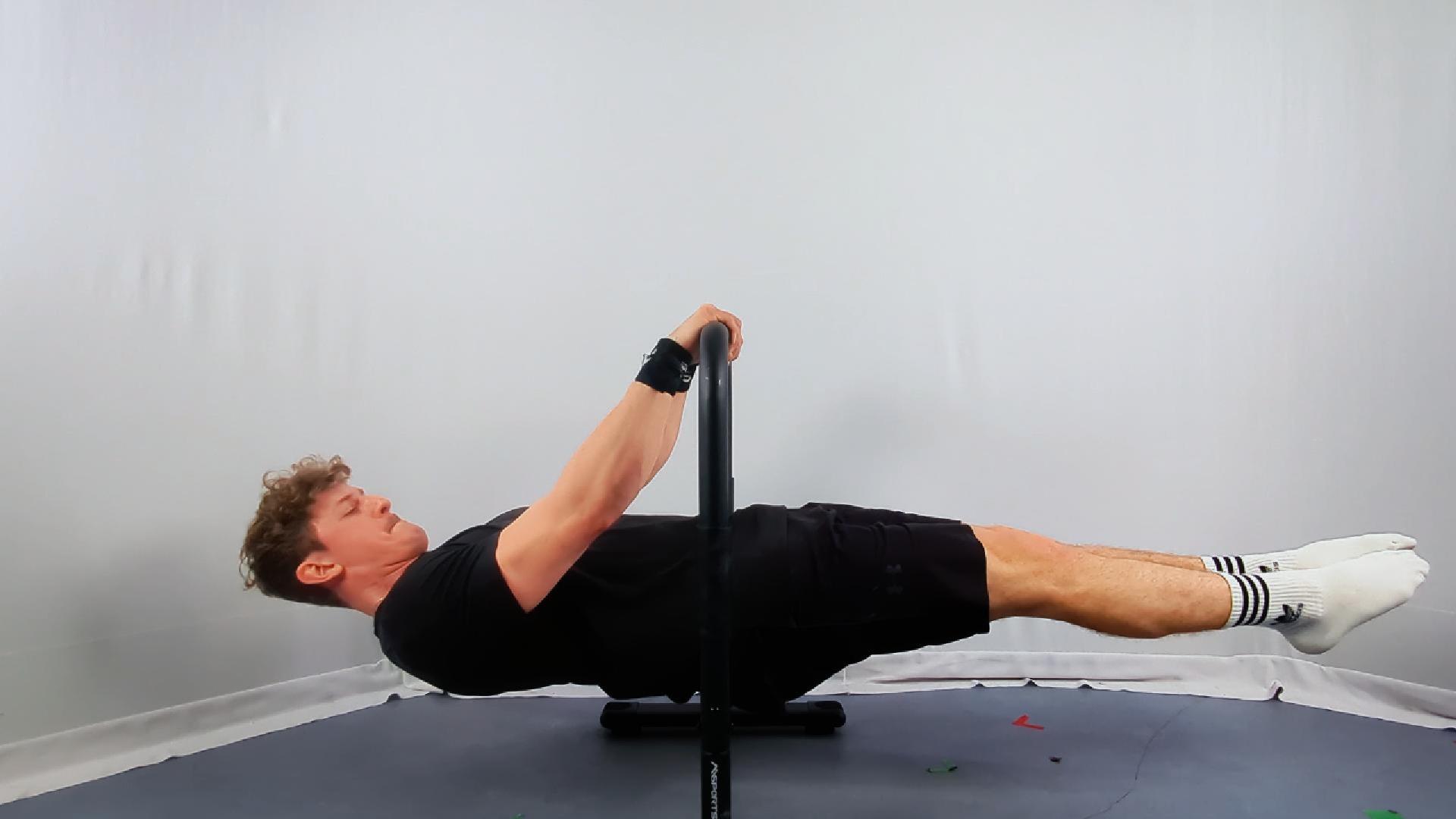 A person performs a calisthenics full front lever hold on parallel bars in a minimalistic indoor setting.