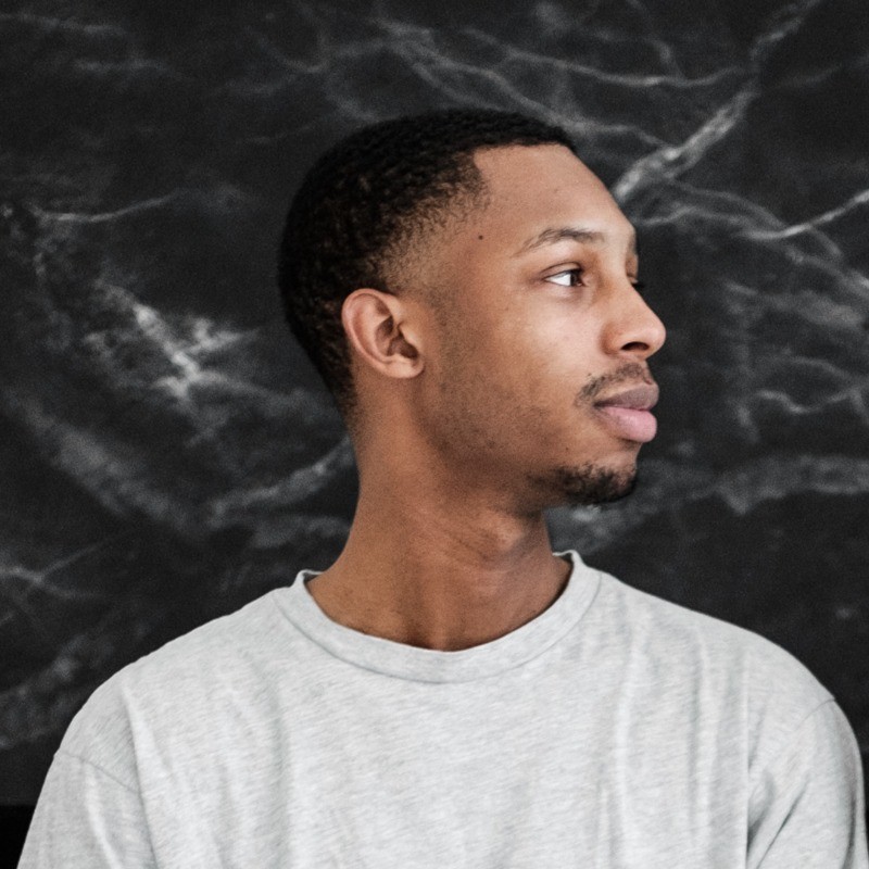 A woman with short curly hair wearing a black t-shirt looks into the camera.