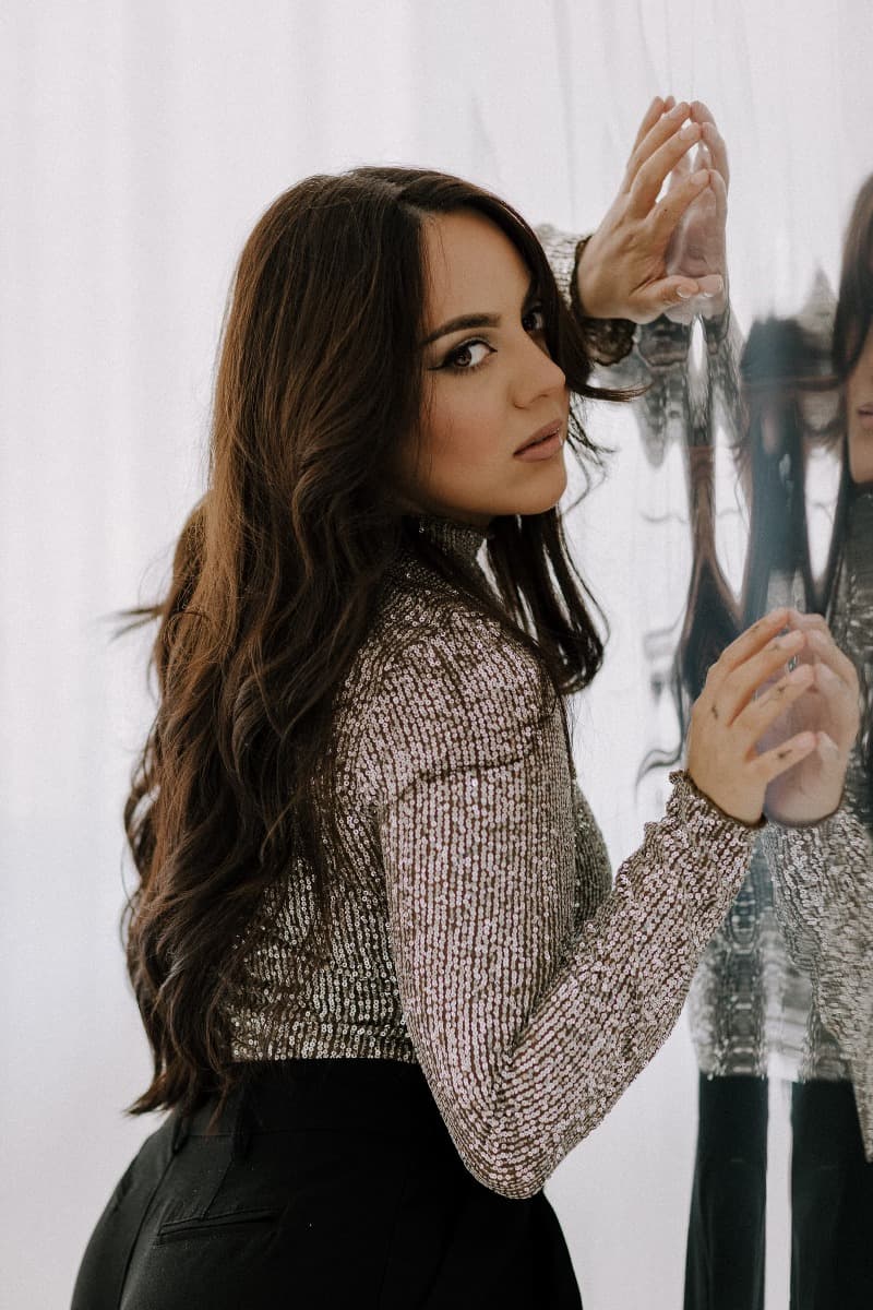 A model leaning against a reflective surface, wearing a sparkling silver top, captured during a creative Mylar shoot at Revelator Studio, a Shreveport natural light studio.