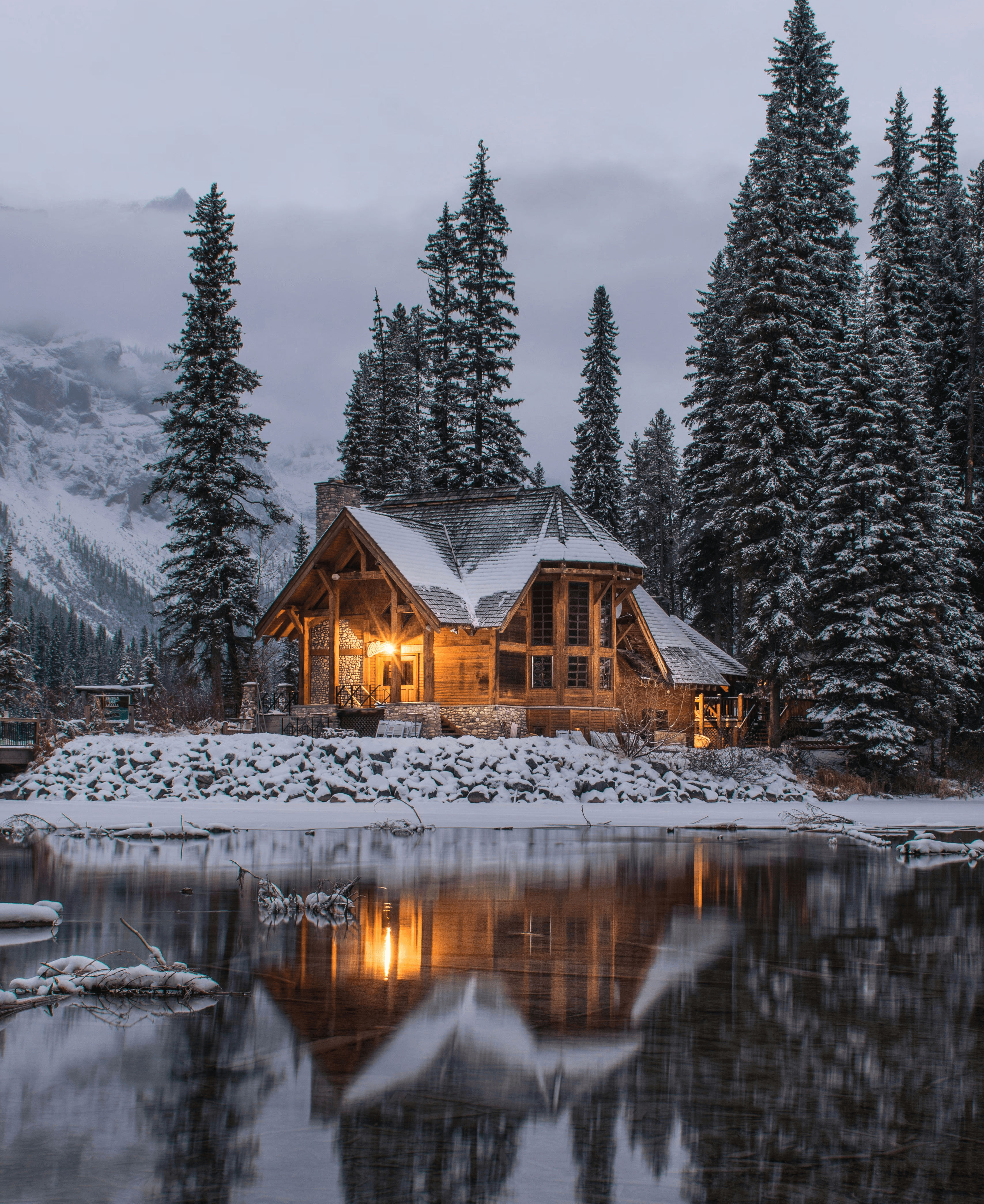 wooden house near pine trees and pond coated with snow during daytime
