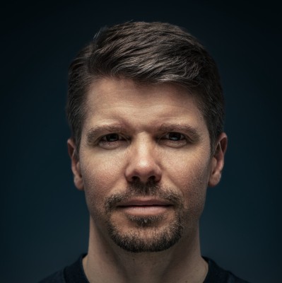 Close-up portrait of a blonde woman in translucent pink glasses and a white shirt on a soft blue background.