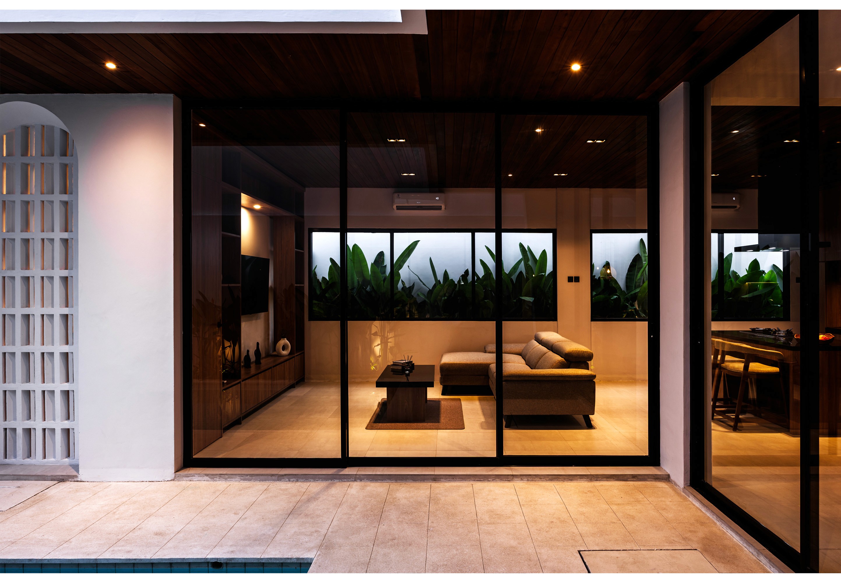 Modern villa lounge with glass doors, tropical foliage view, and ambient lighting at dusk.