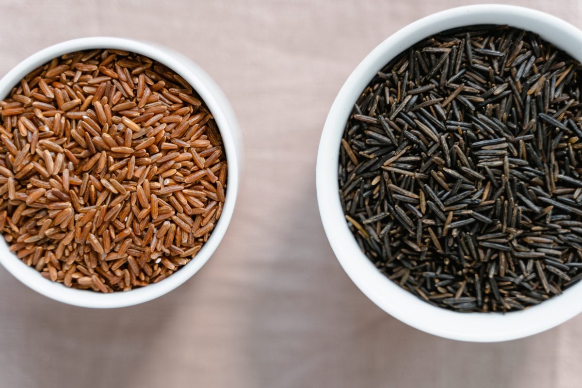 Two bowls of black and brown rice sit in white bowls.