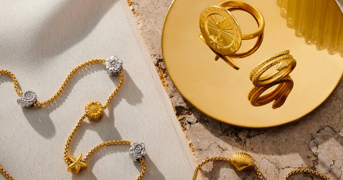 Gold jewelry pieces displayed on a beige fabric and stone surface, with rings placed on a golden dish.
