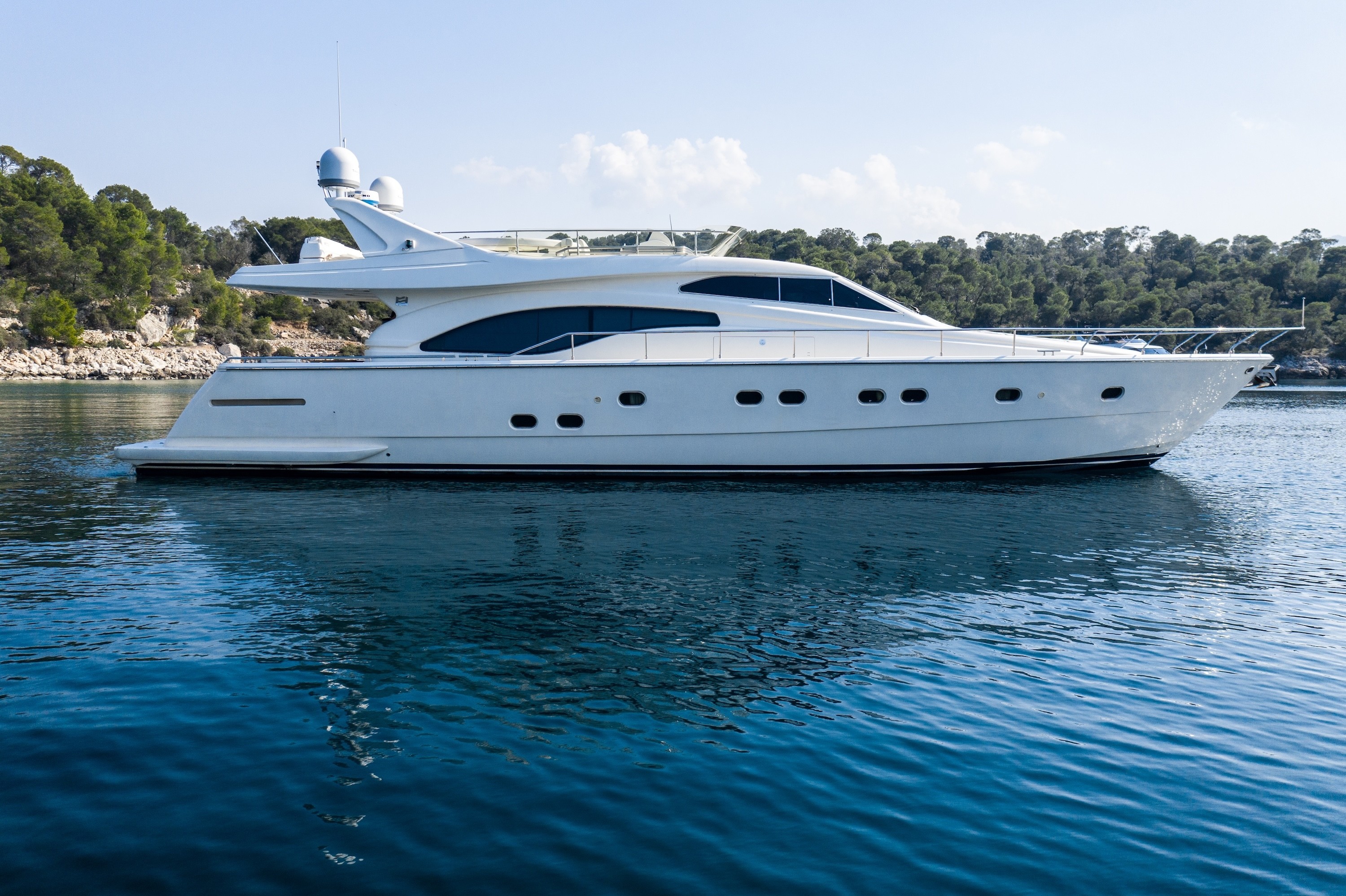 White Ferretti 68 motor yacht anchored in calm blue waters near a forested Mediterranean coastline.