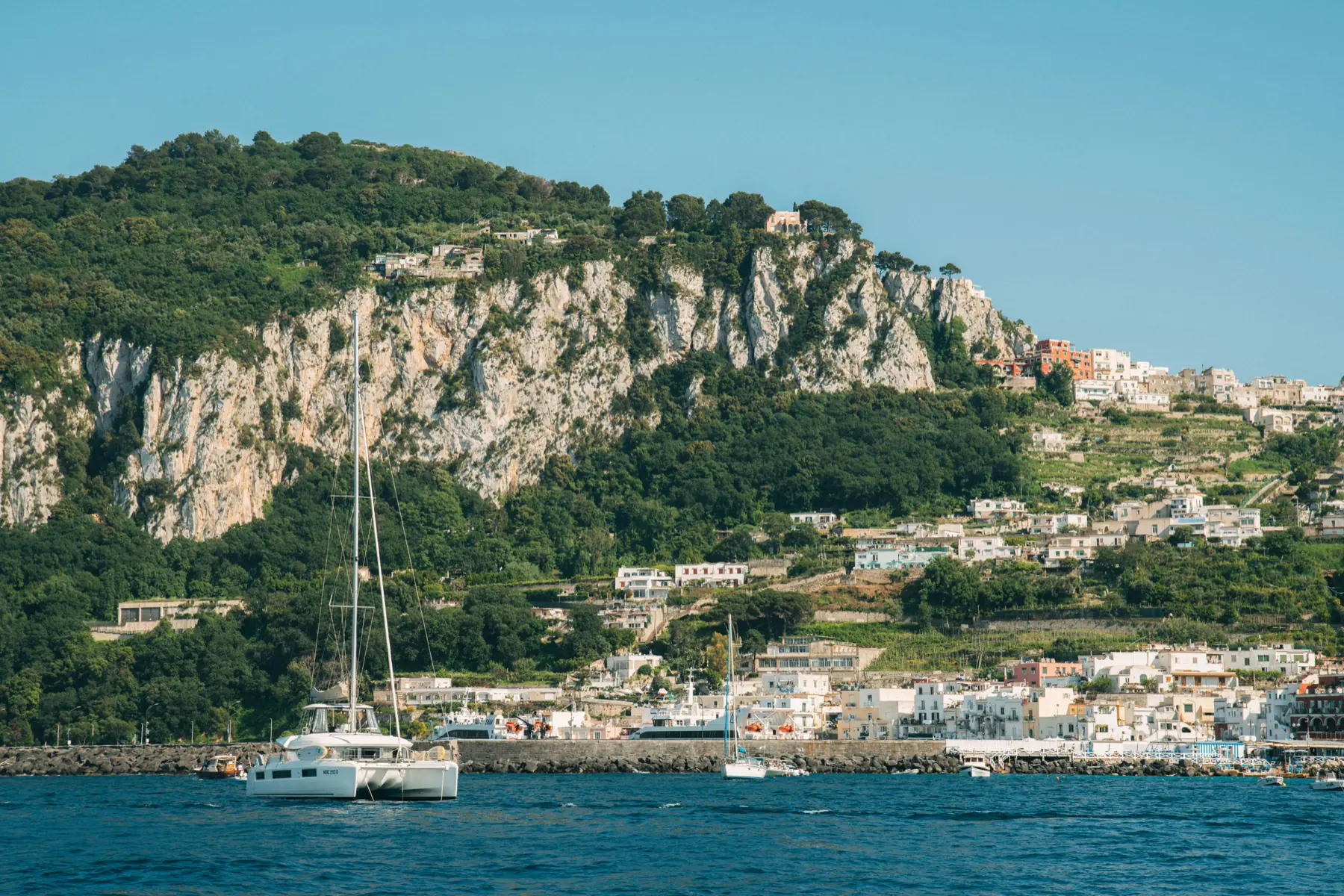 Catamaran de location naviguant près d’une ville insulaire méditerranéenne