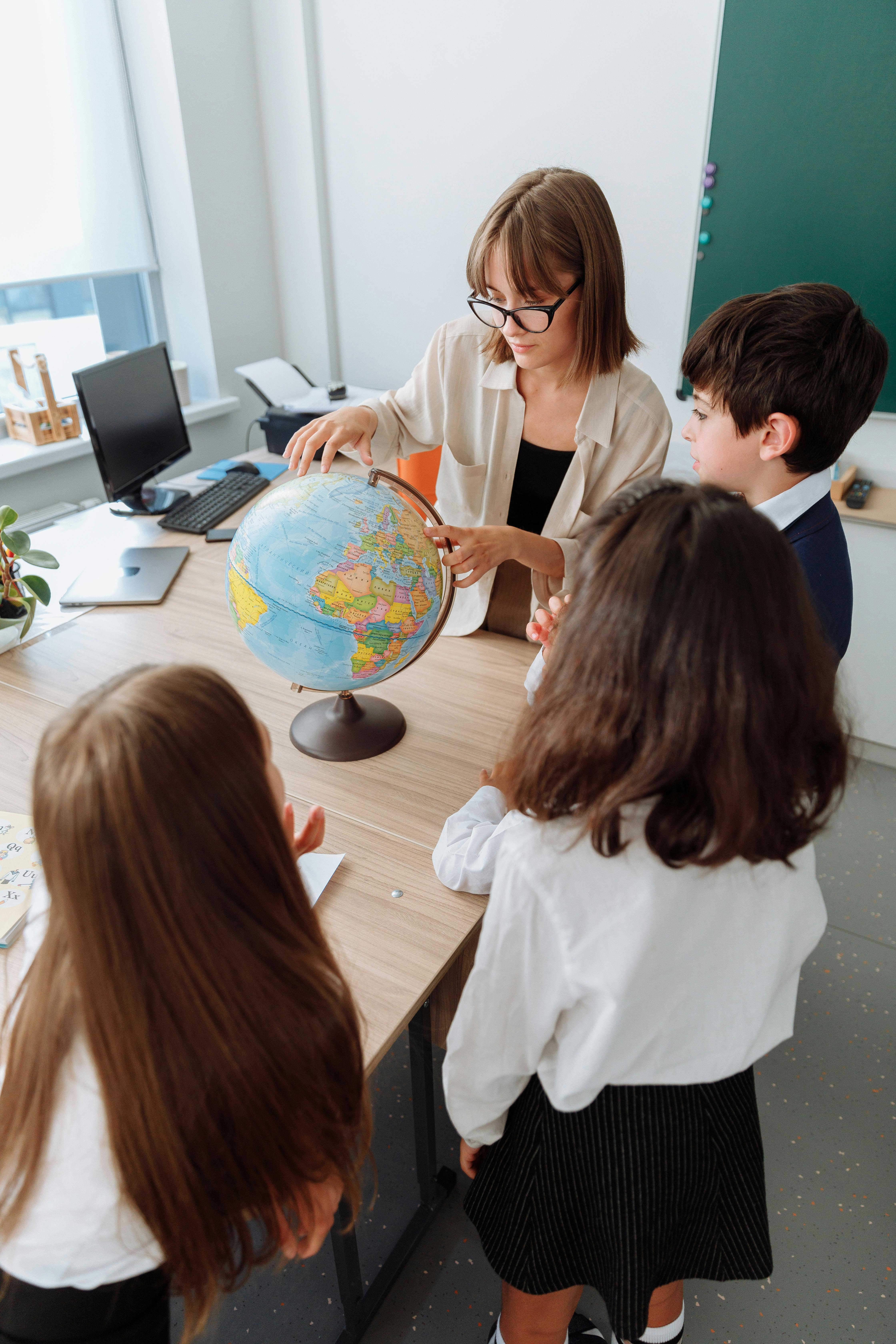 A teacher is showing a globe to a group of students, pointing to different locations as the students watch attentively