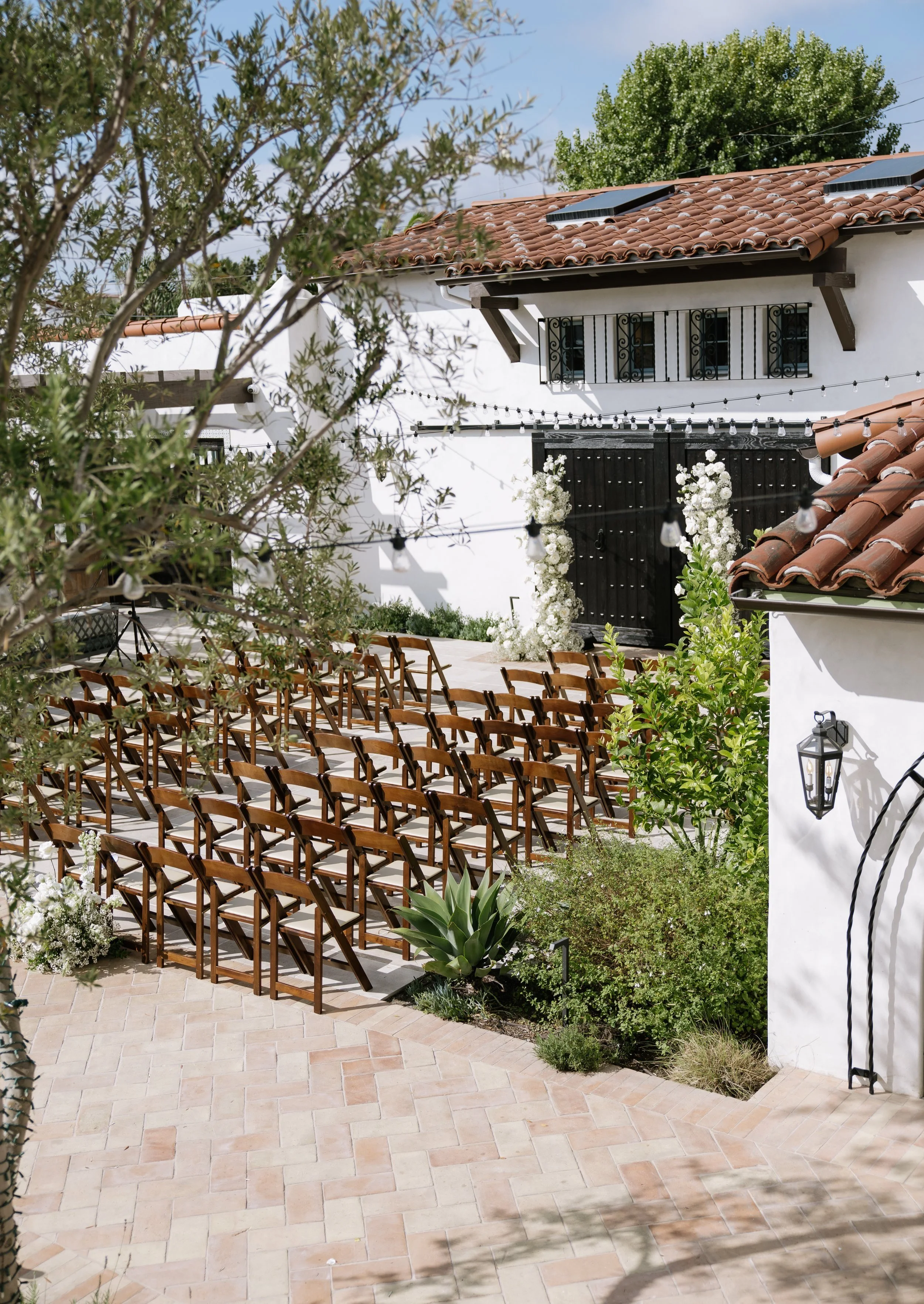 A serene outdoor wedding setup with white chairs arranged on green grass under a canopy of trees.