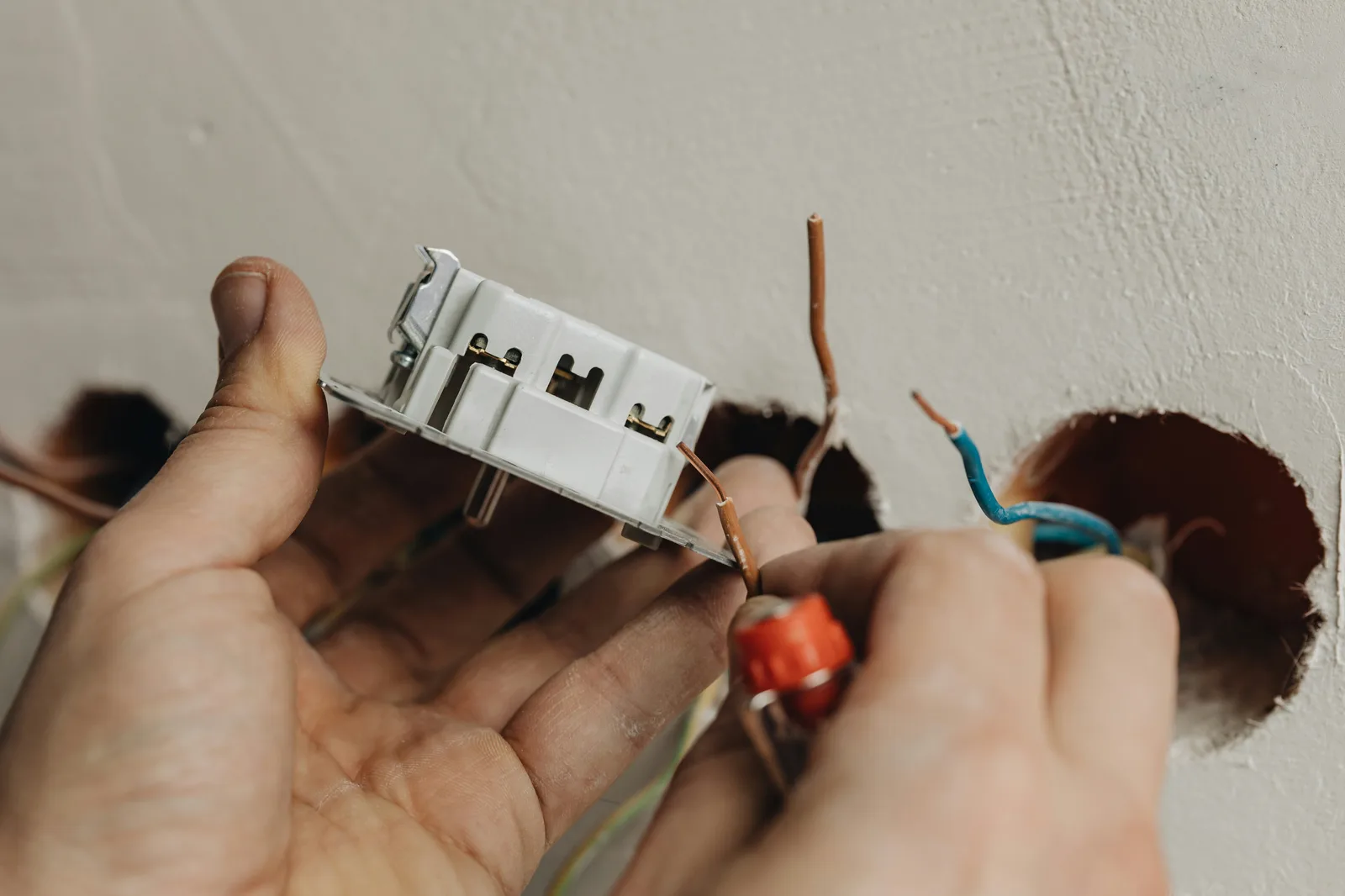 Hands wiring an electrical outlet mechanism with exposed copper wire
