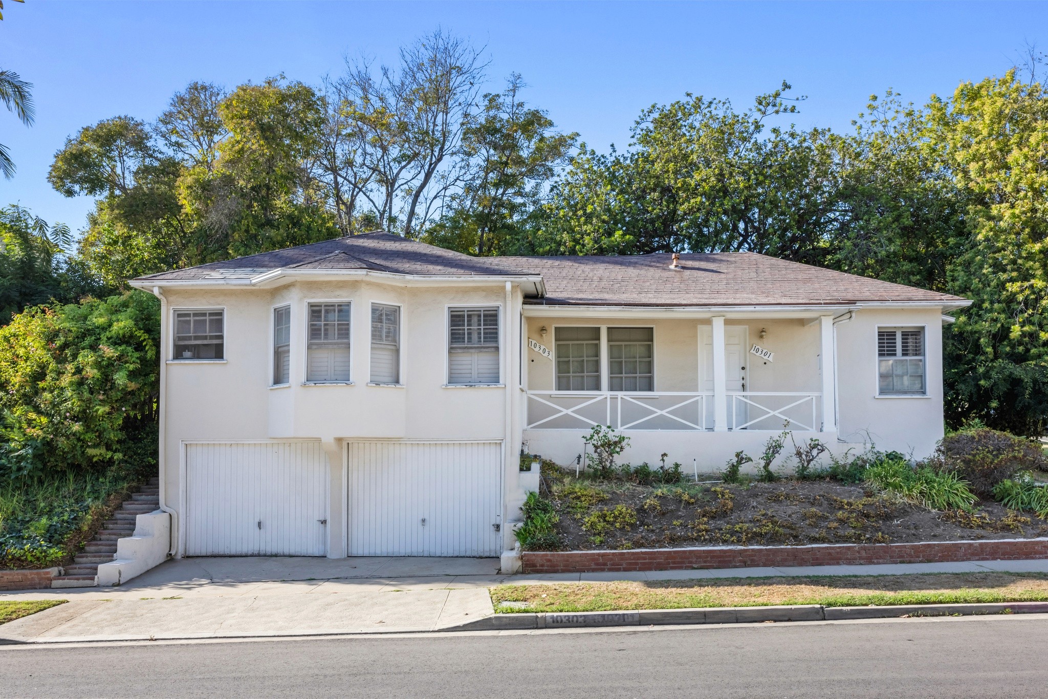 A white single-story duplex at 10301 mississippi, with a small front yard, surrounded by greenery, under a clear blue sky.