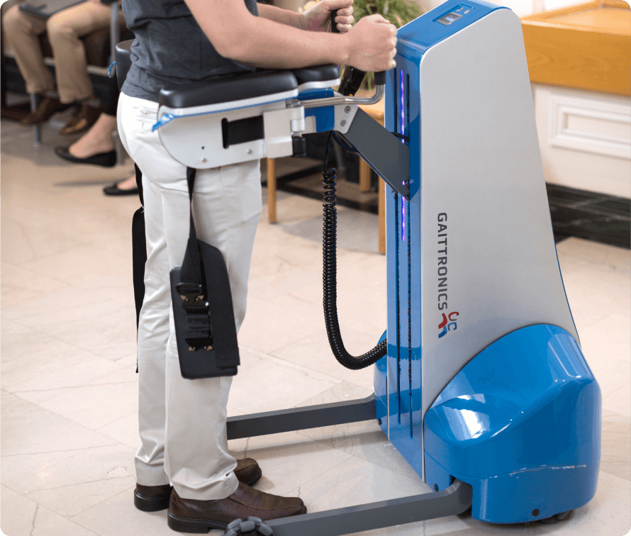 Person using a robotically assisted walker, walking with support, showcasing the device's ergonomic design and mobility-enhancing features.