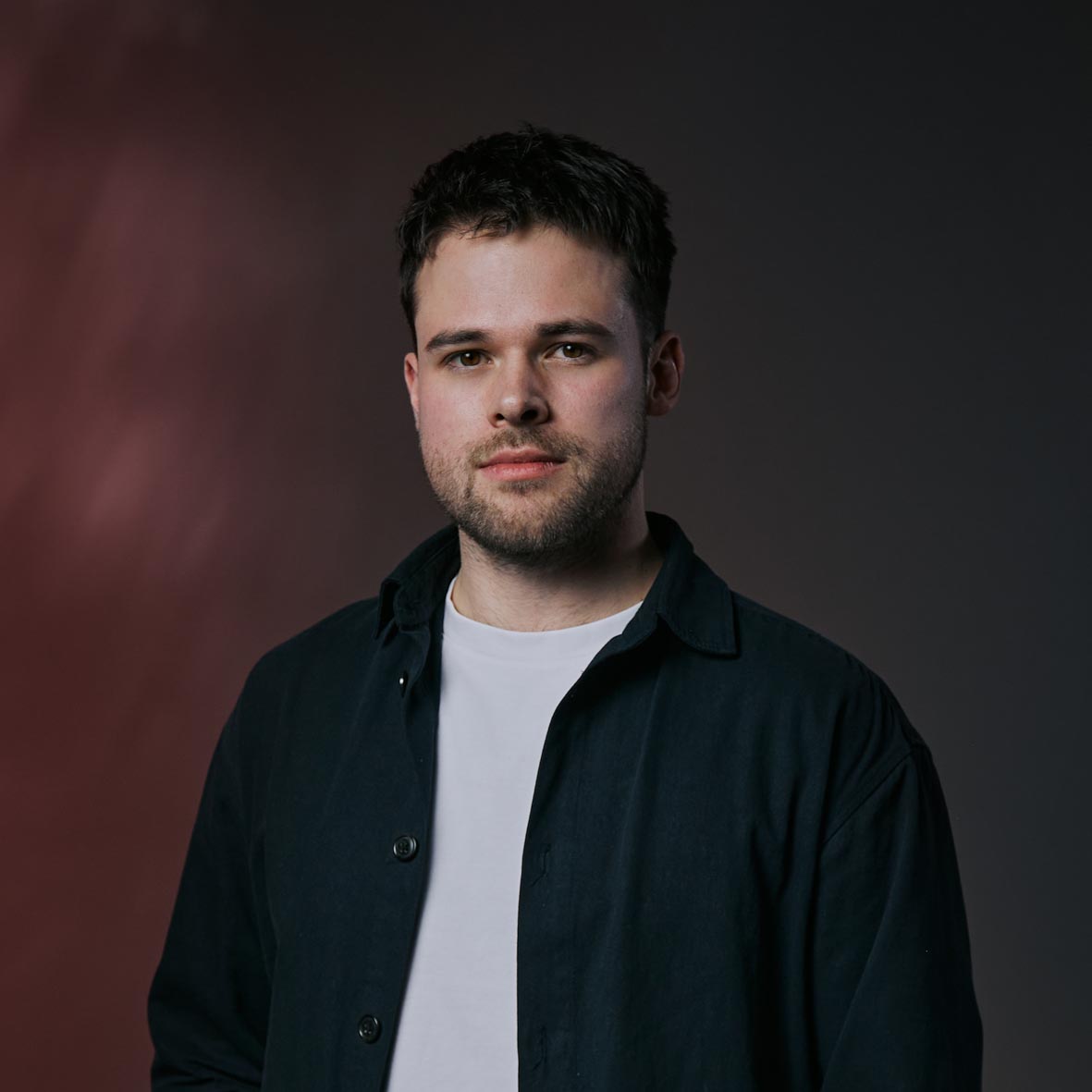 A young woman with long dark hair smiles confidently while crossing her arms in a modern indoor setting.
