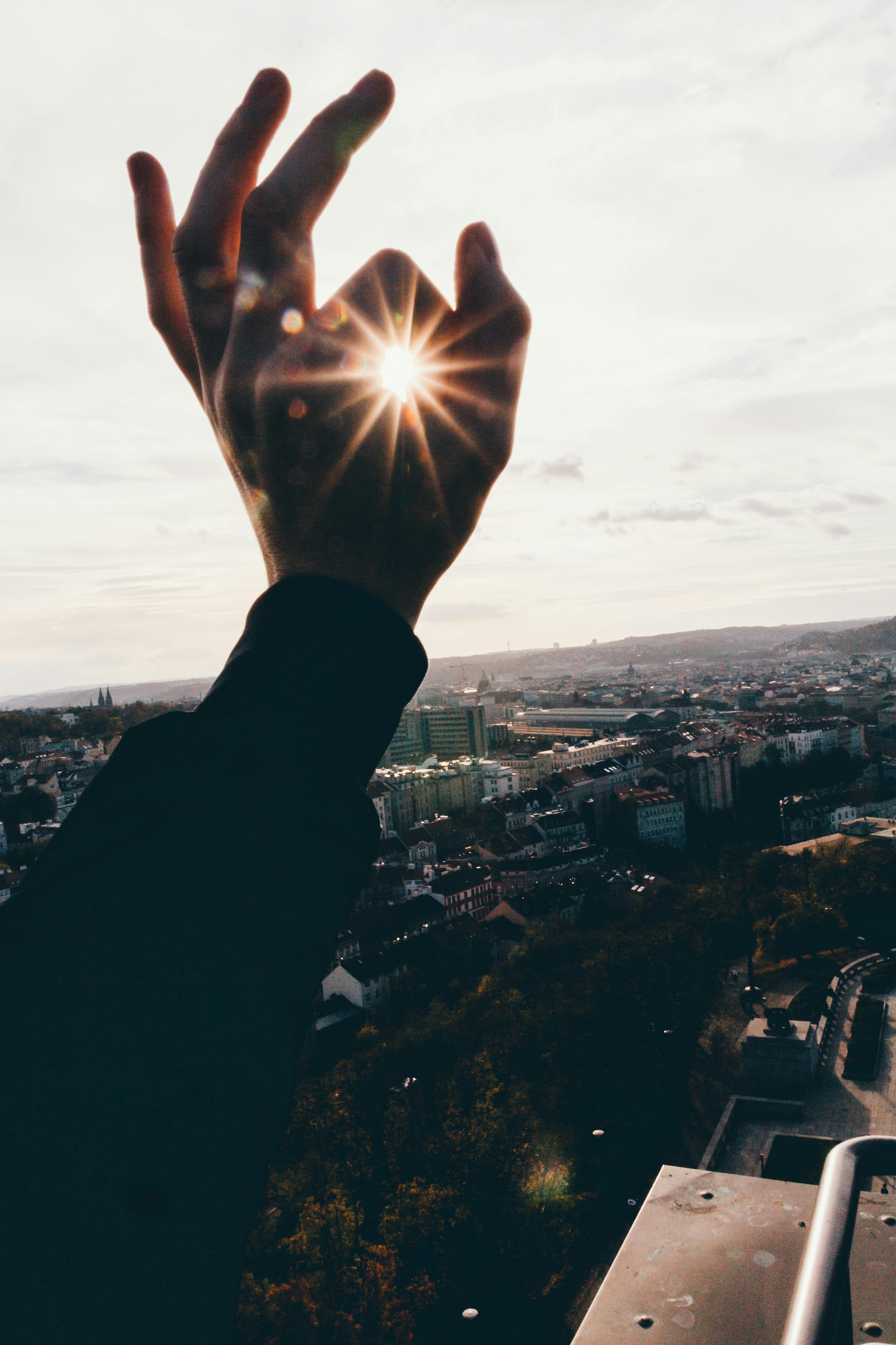 Silhouette of a hand held up to the sky, with index finger pressed to thumb to create a circle and the sun shining through the circle