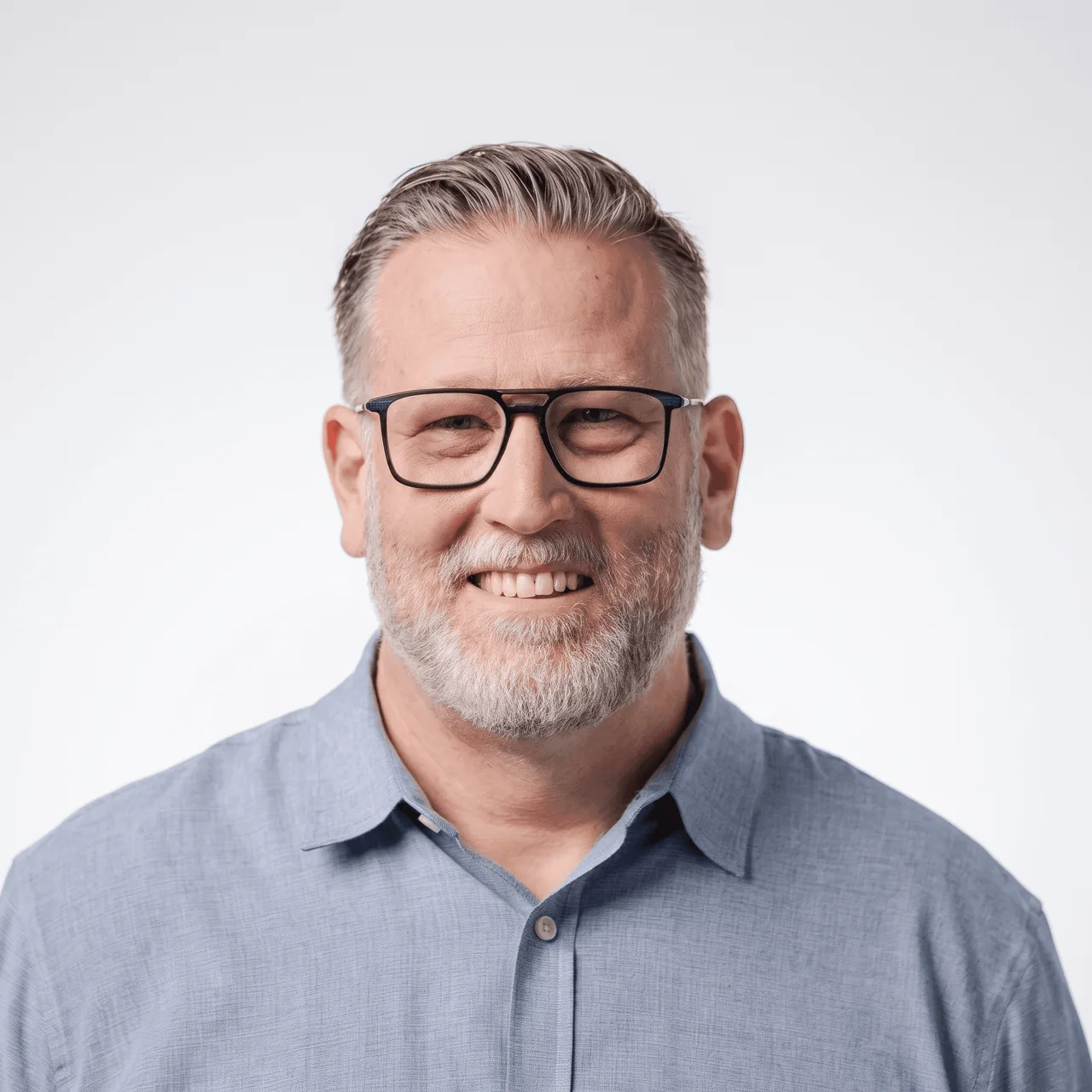 A smiling man with glasses and gray hair sits in a bustling cafe, surrounded by people and workspaces.