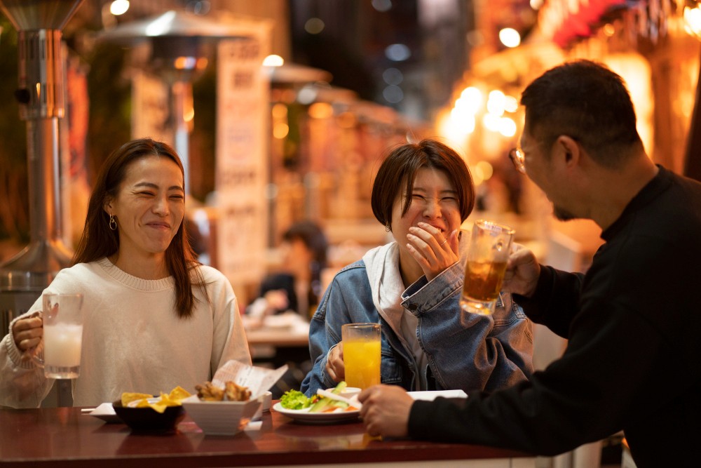香港商業保險服務為餐飲食肆提供店舖保險，三人在燈火璀璨的戶外餐廳愉快舉杯暢飲。