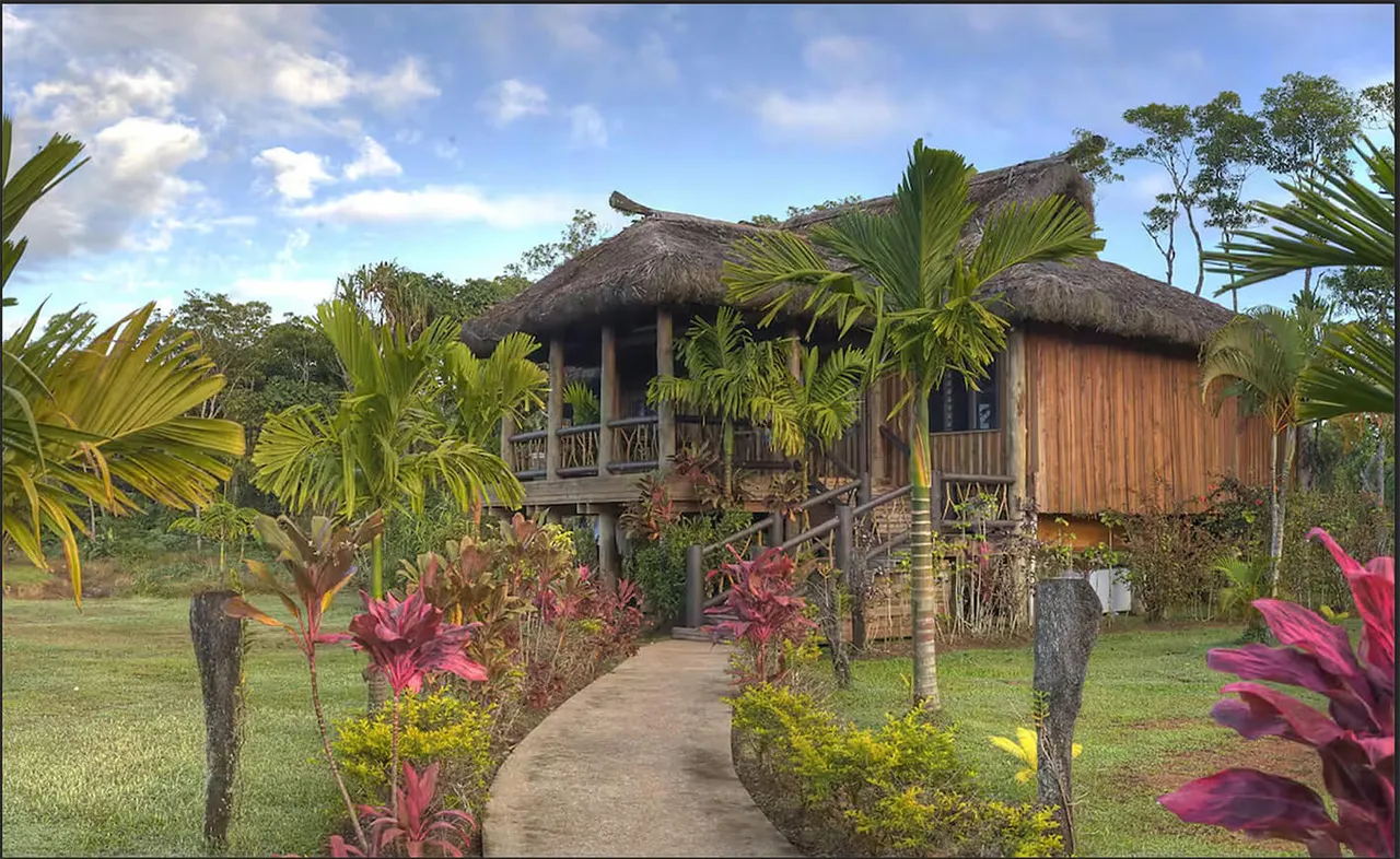 A traditional Fijian bure with thatched roof and wooden balcony, surrounded by tropical plants at Uprising Beach Resort.