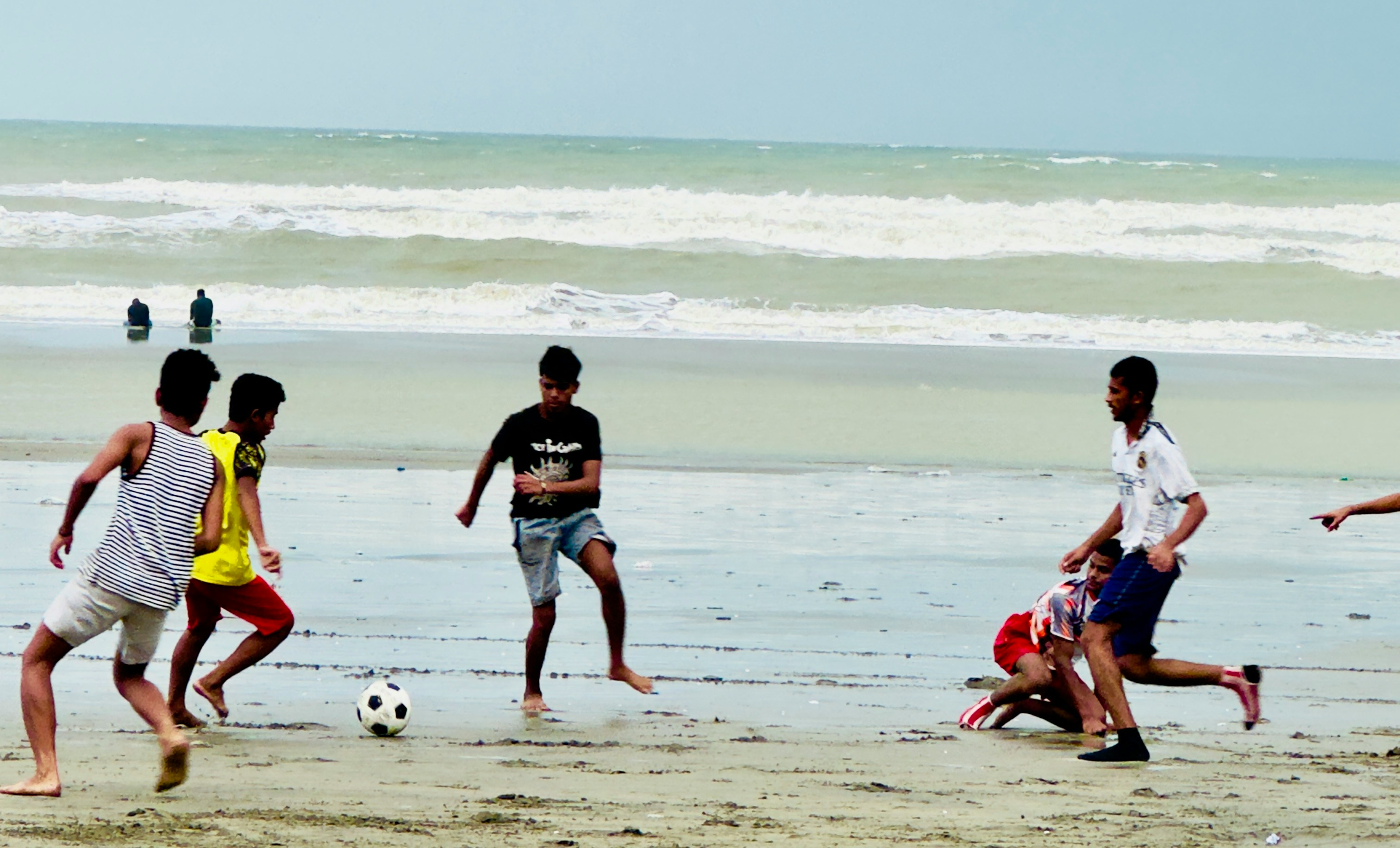 Young men playing soccer on a sandy beach.