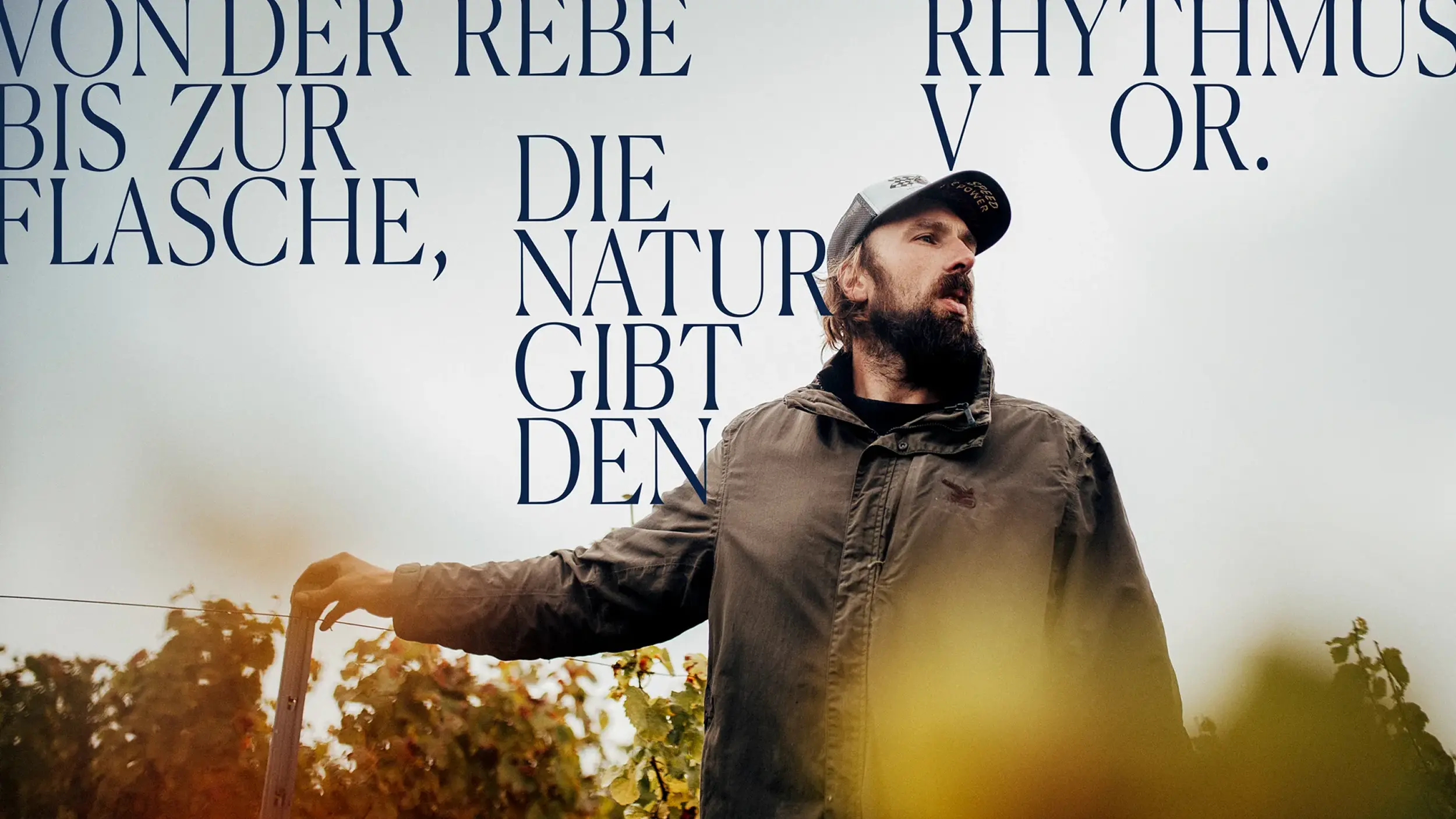 Winzer im Weinberg vor dem Slogan „Von der Rebe bis zur Flasche, die Natur gibt den Rhythmus vor.“