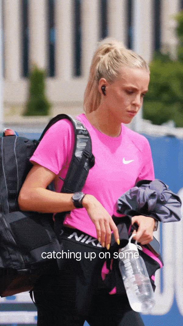 Model holding a piece of wheat in a field, gazing downward.