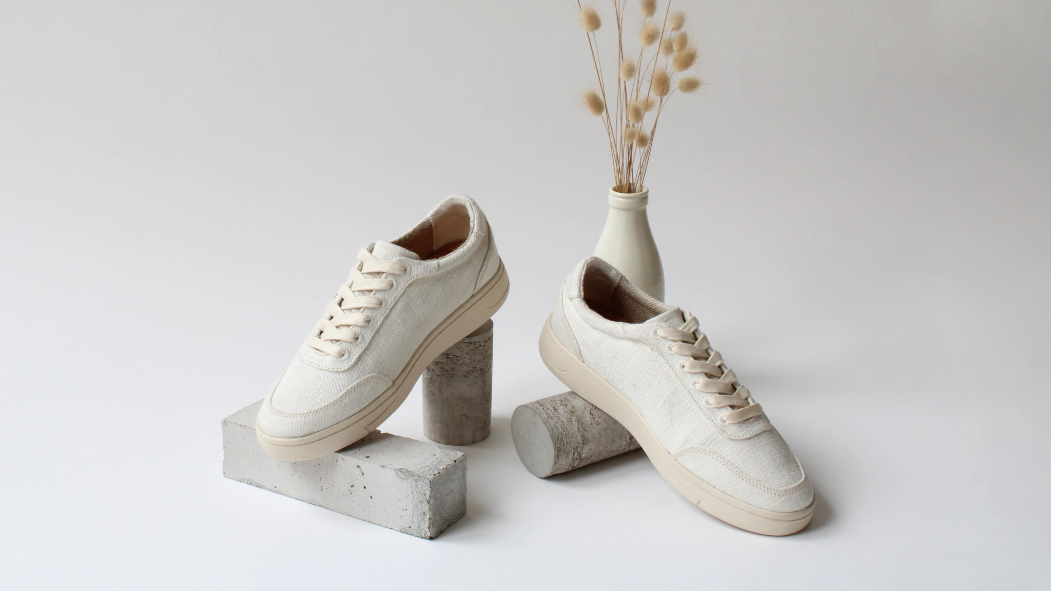 A pair of off-white Orba Ghost plant-based sneakers balanced on small concrete blocks.