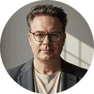 A man wearing glasses and a suit jacket, looking confidently at the camera.