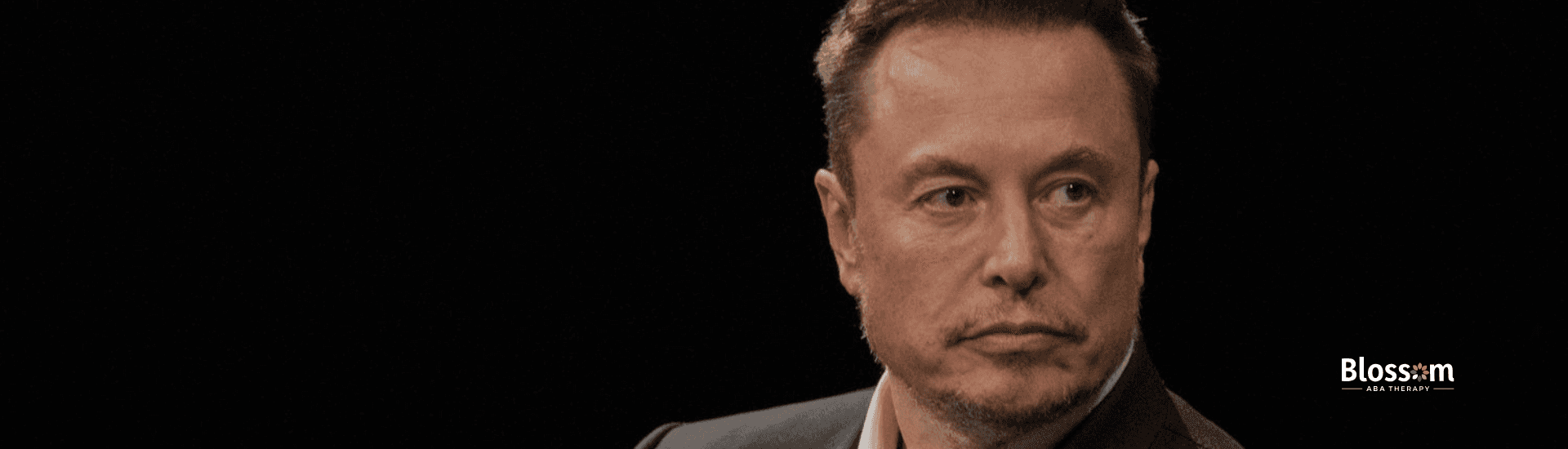 Elon Musk, diagnosed w/ autism, in a black suit sitting on stage in Virginia, looking contemplative.