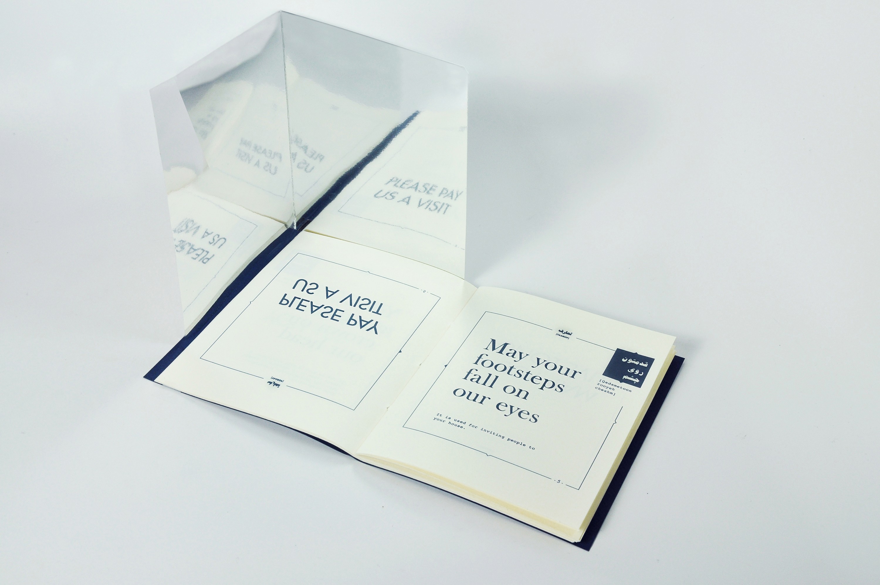 A photo of an opened book with some sort of corner mirror placed near it. On the page near the mirrors there is the text: Please pay us a visit. This is written so it will be only visible from the mirror. The other text reads: May it become meat on your body.