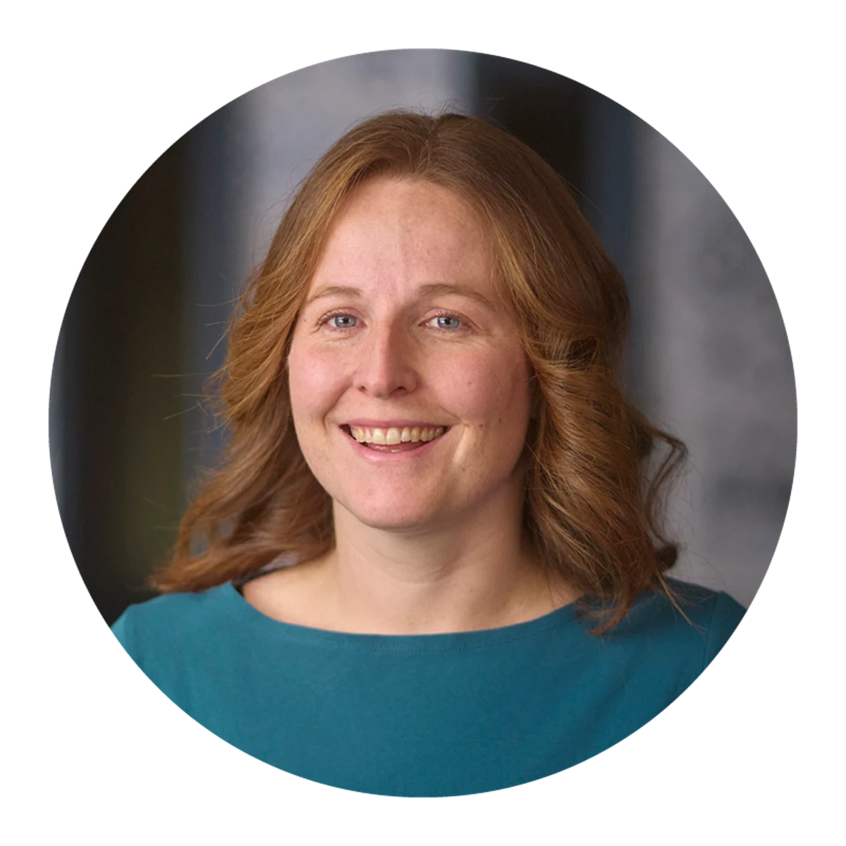 Person with shoulder-length wavy hair wearing a teal top in a professional setting.