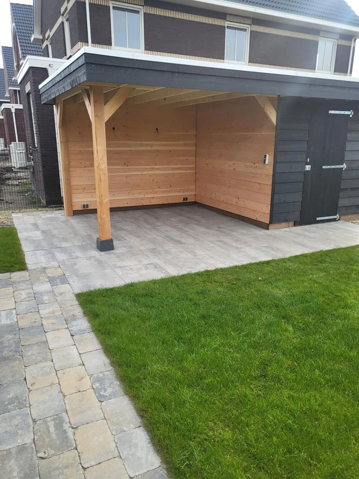 Hoekoverkapping met houten wanden en zwarte berging in achtertuin in omgeving Gorredijk en Heerenveen