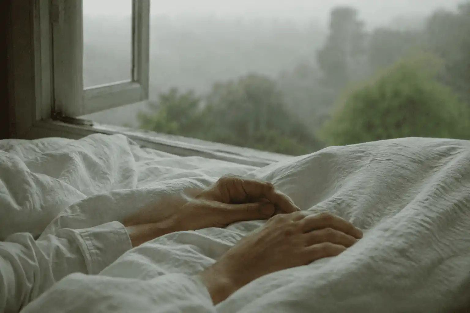 Hands emerging from white sheets with a quiet forest beyond