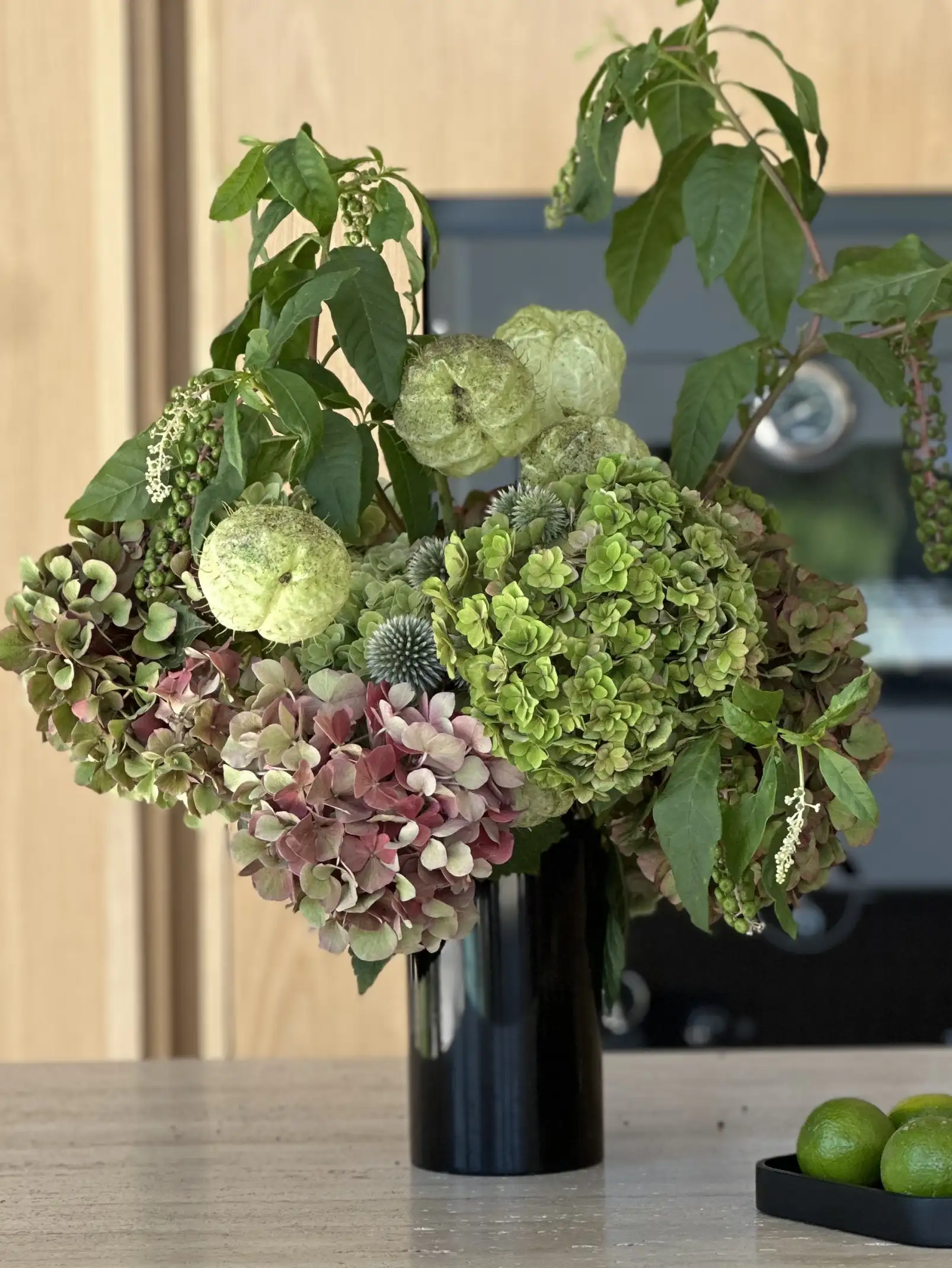 Arreglo floral con hortensias verdes y rosadas en jarrón negro para interioristas que buscan añadir textura y frescura a espacios modernos.