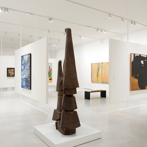 Modern konstgalleriets interiör med abstrakta målningar på vita väggar och en geometrisk skulptur på en piedestal i förgrunden.