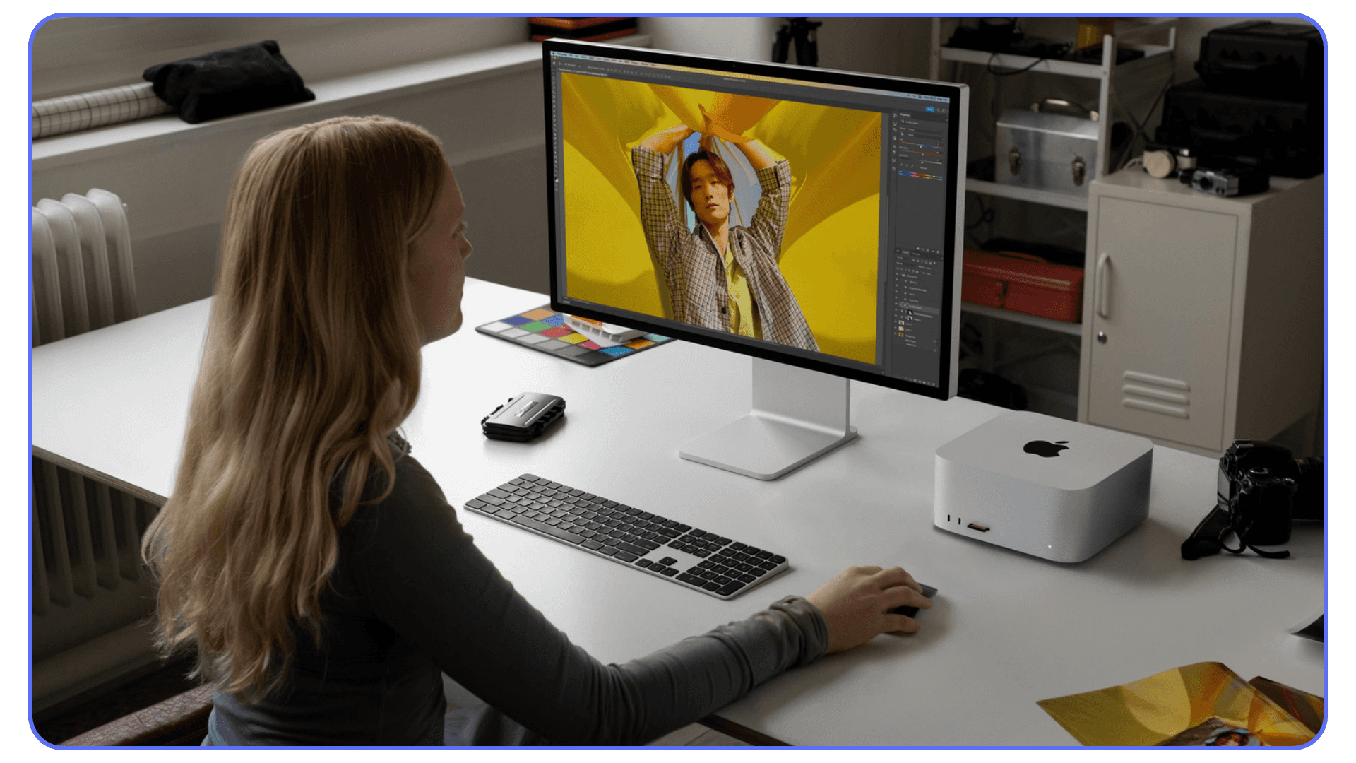 A person editing a photo in Photoshop on a large monitor, with an Apple Mac Mini and keyboard on the desk.
