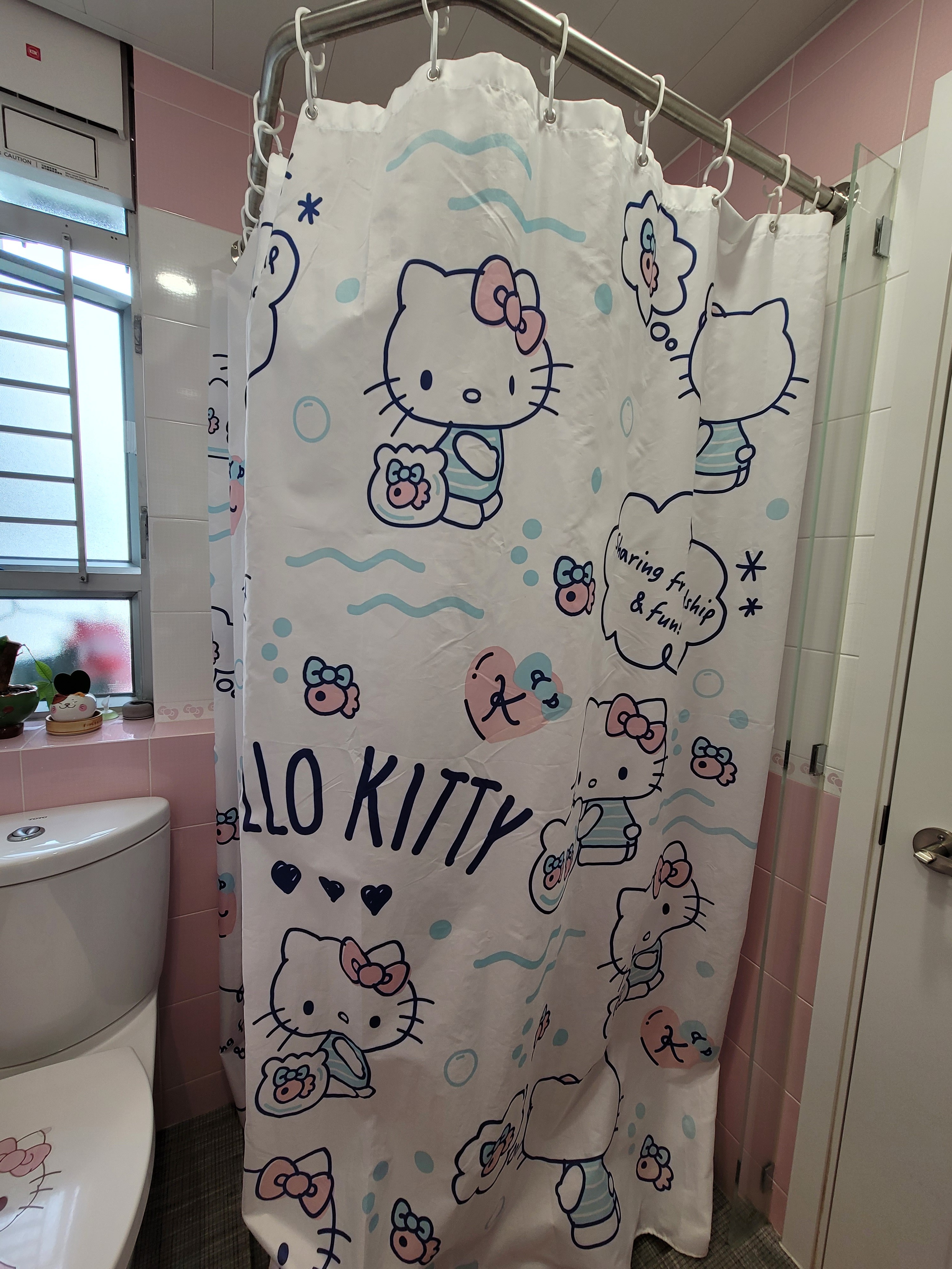 Hello Kitty graphic shower curtain hanging from a curved metal rod in a pink-tiled bathroom design simple at Hoi Tat Estate.