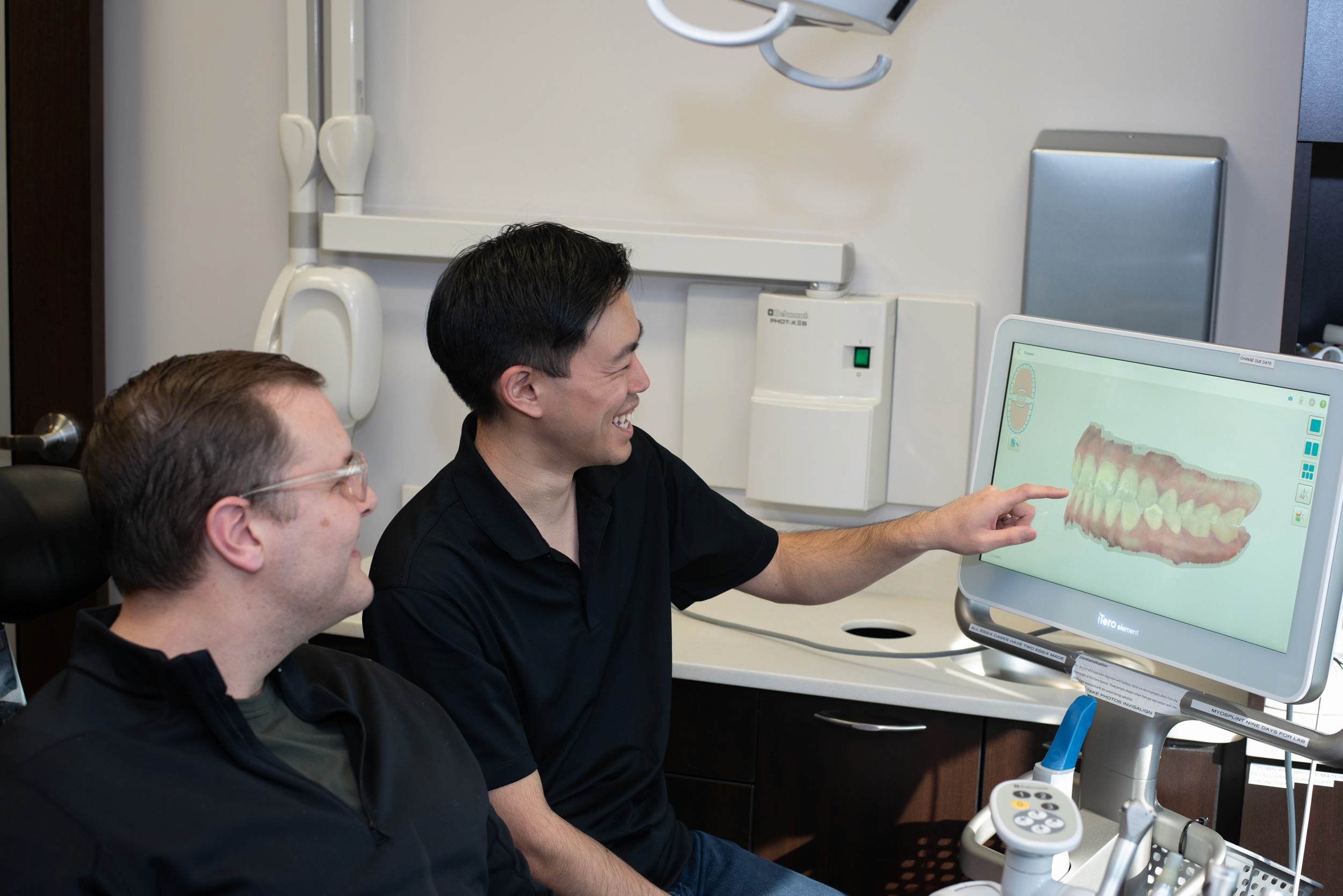 Dentist showing a male patient a digital 3D model of teeth on a screen during a consultation in a modern dental office.