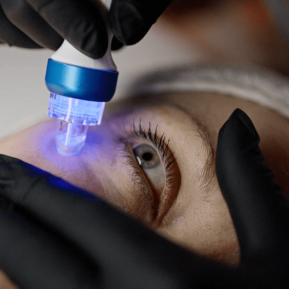 Woman wearing a sheet mask and using a jade roller at a vanity table, surrounded by skincare products