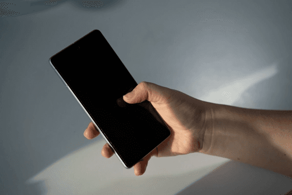 빛이 비치는 실내에서 검은색 스마트폰을 한 손으로 쥐고 조작하는 모습입니다.