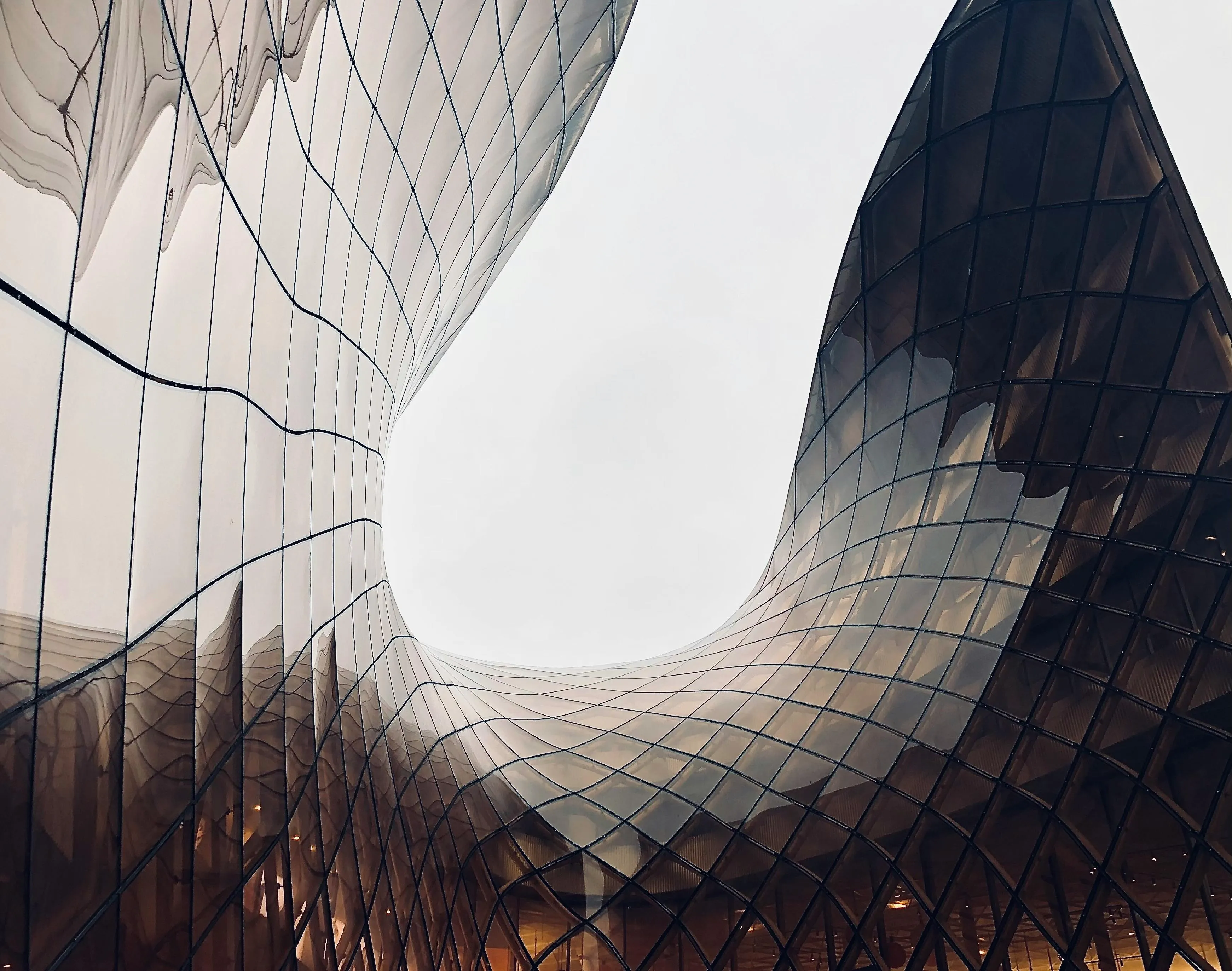 Abstract architectural detail showcasing a curved glass facade with a geometric grid pattern reflecting a bright sky.