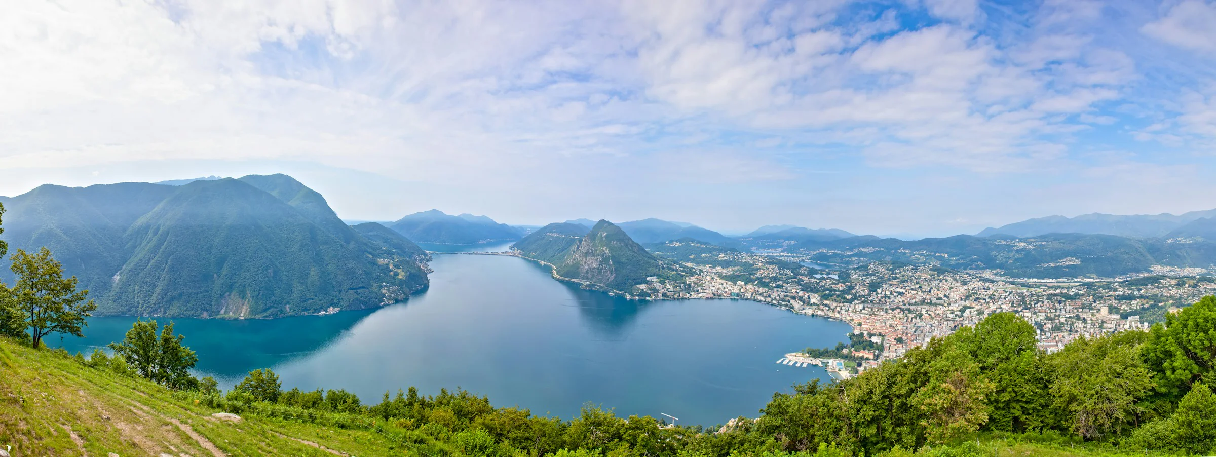 Lugano, Luganersee mit Stadt und Monte San Salvatore aus der Höhe bei blauem Himmel