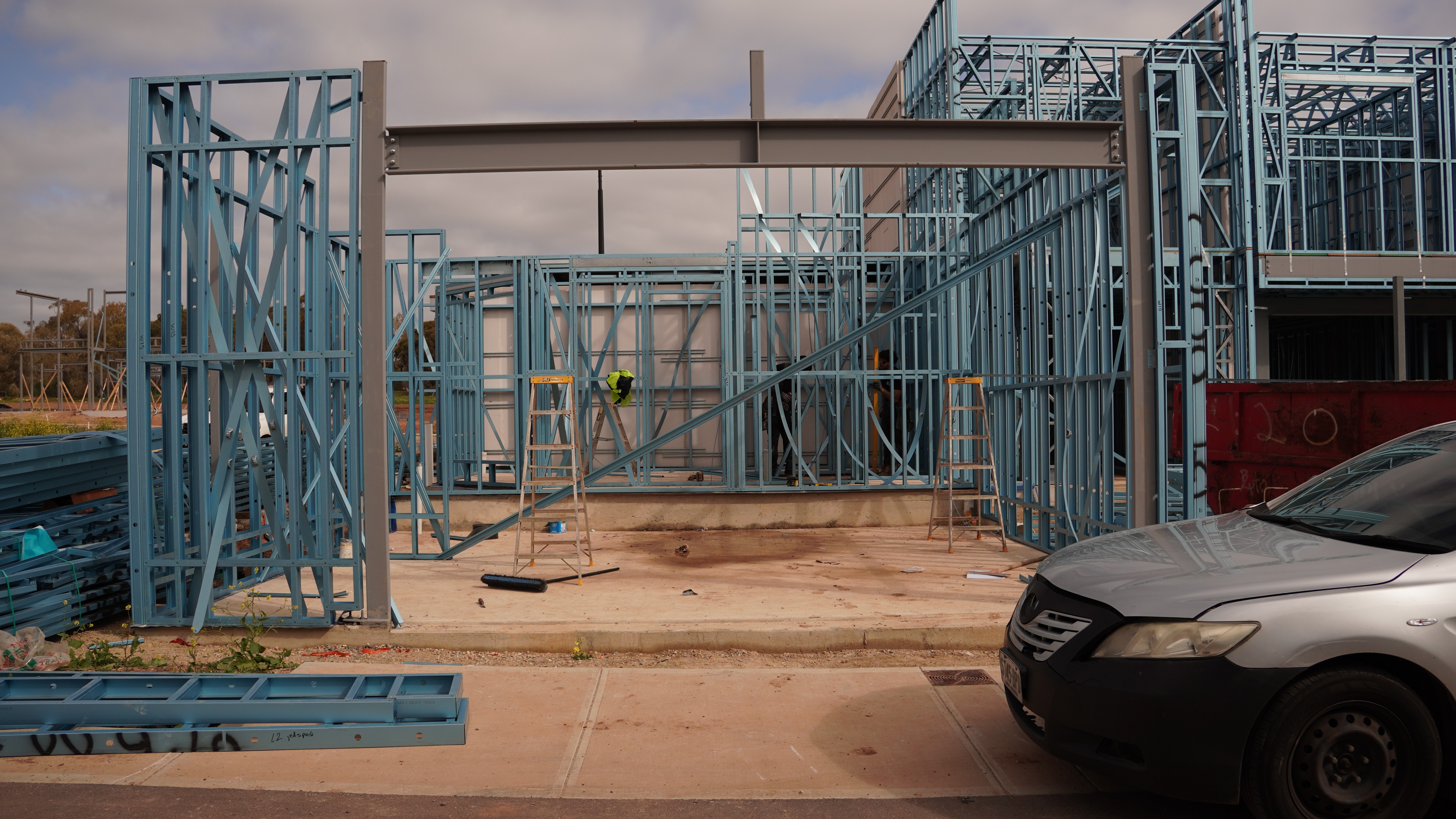Smiling young woman with long hair standing against a dark green background, holding a finger to her chin.